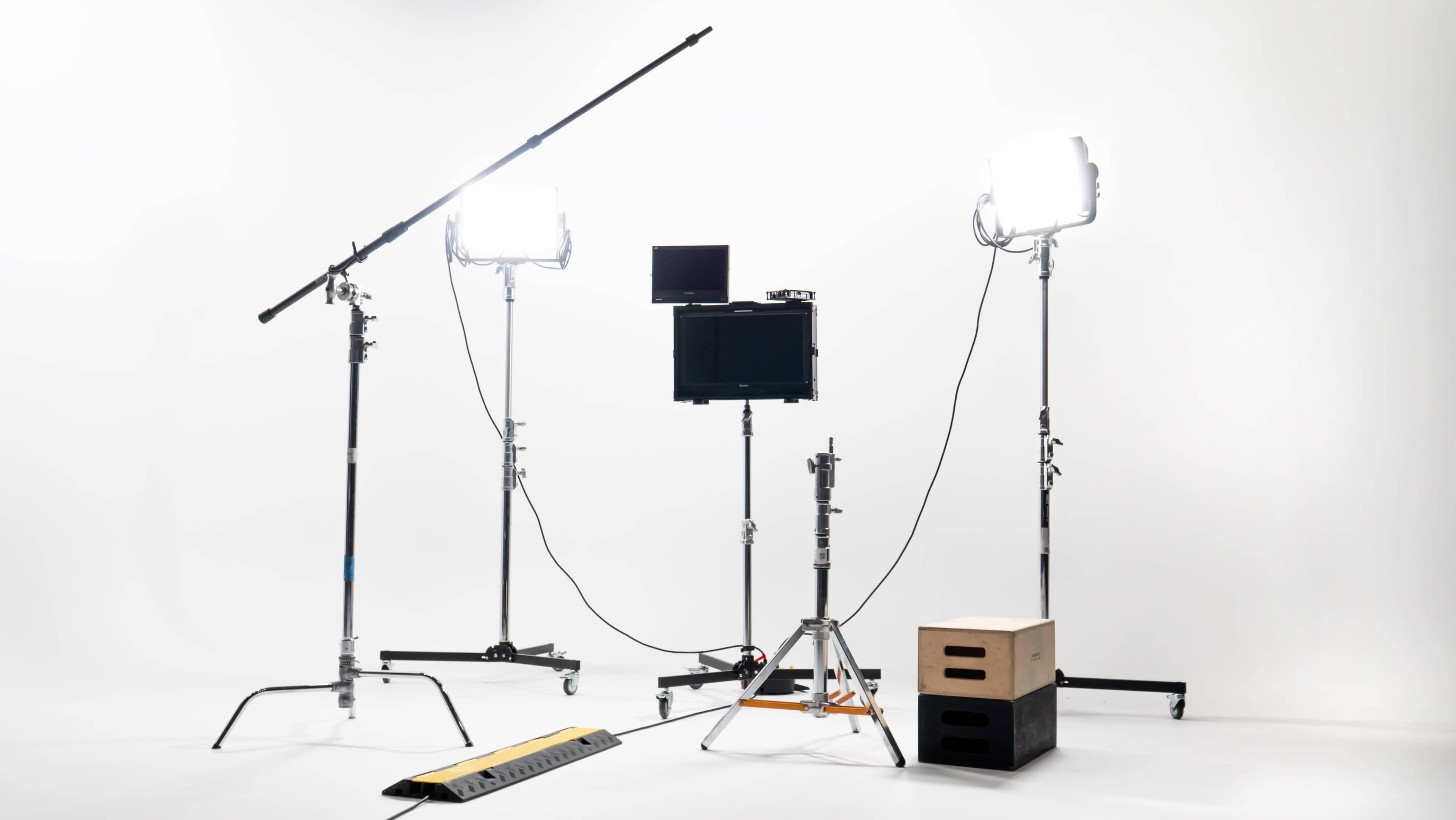 A photography setup with two lighting stands, a monitor on a tripod, and a few equipment boxes on a plain white background.