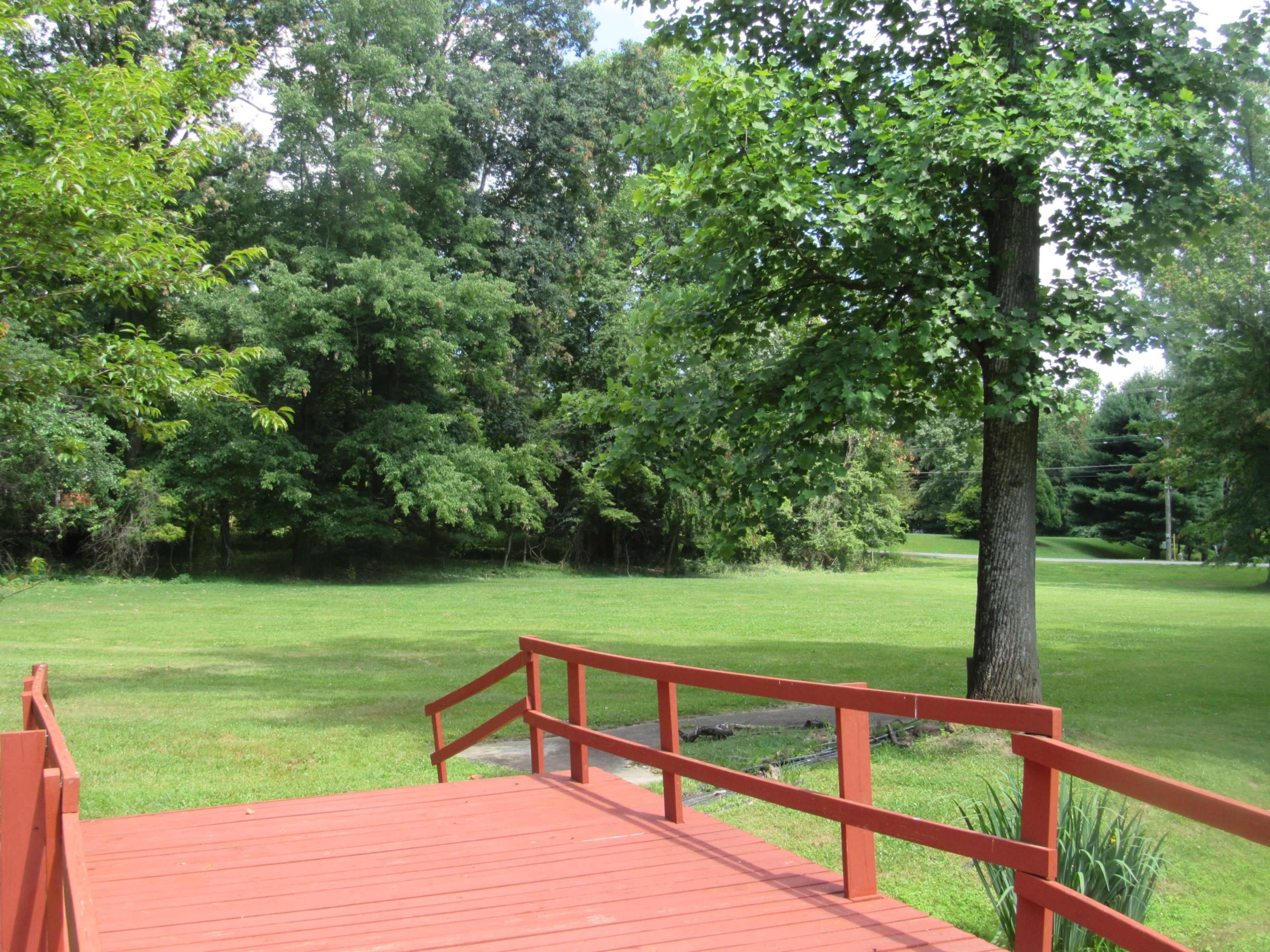 A red wooden deck overlooks a grassy yard surrounded by trees.