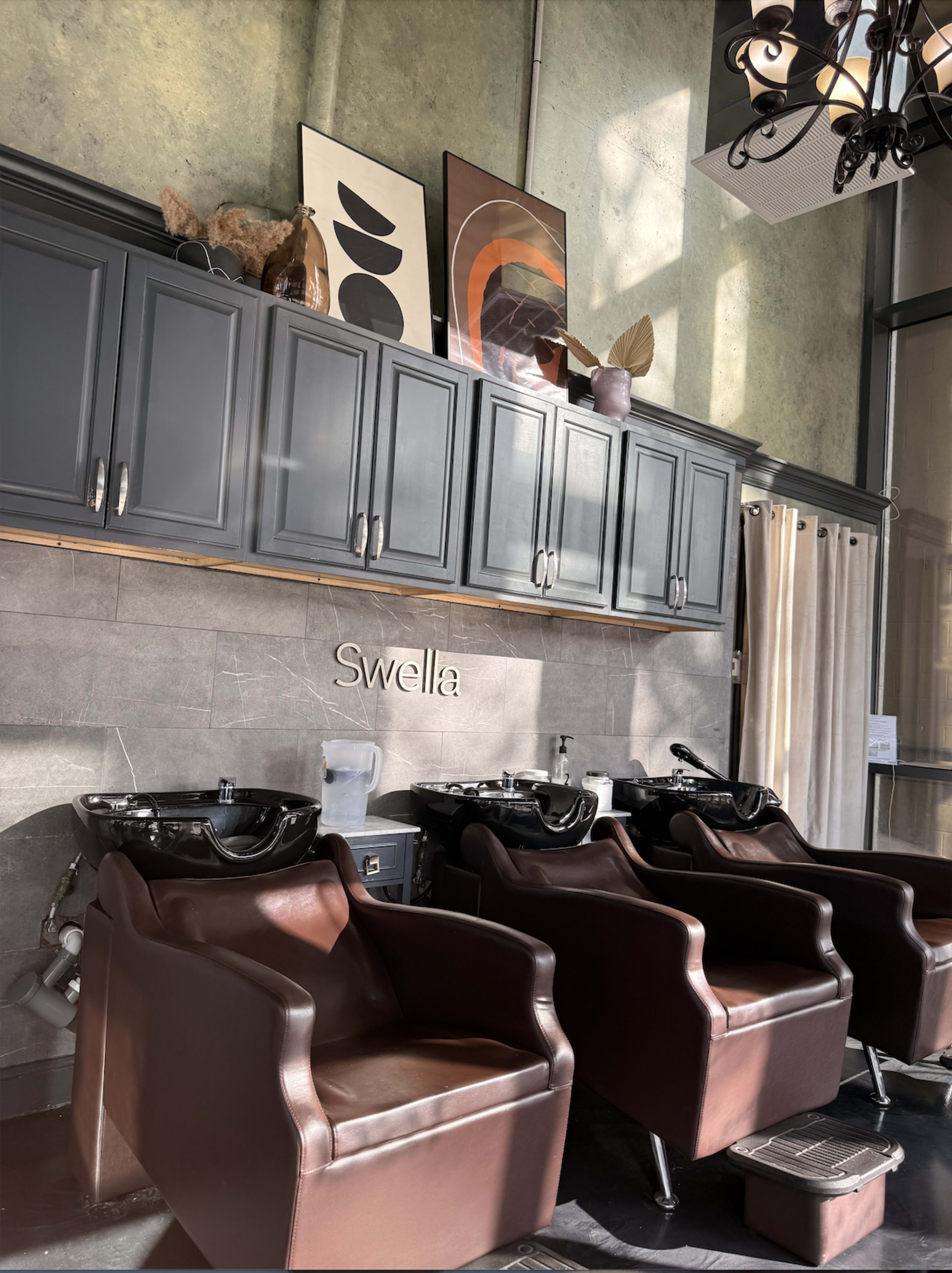 The image shows a modern hair salon interior featuring brown styling chairs, a decorated wall with artwork, and a prominent sign that reads "Swella."