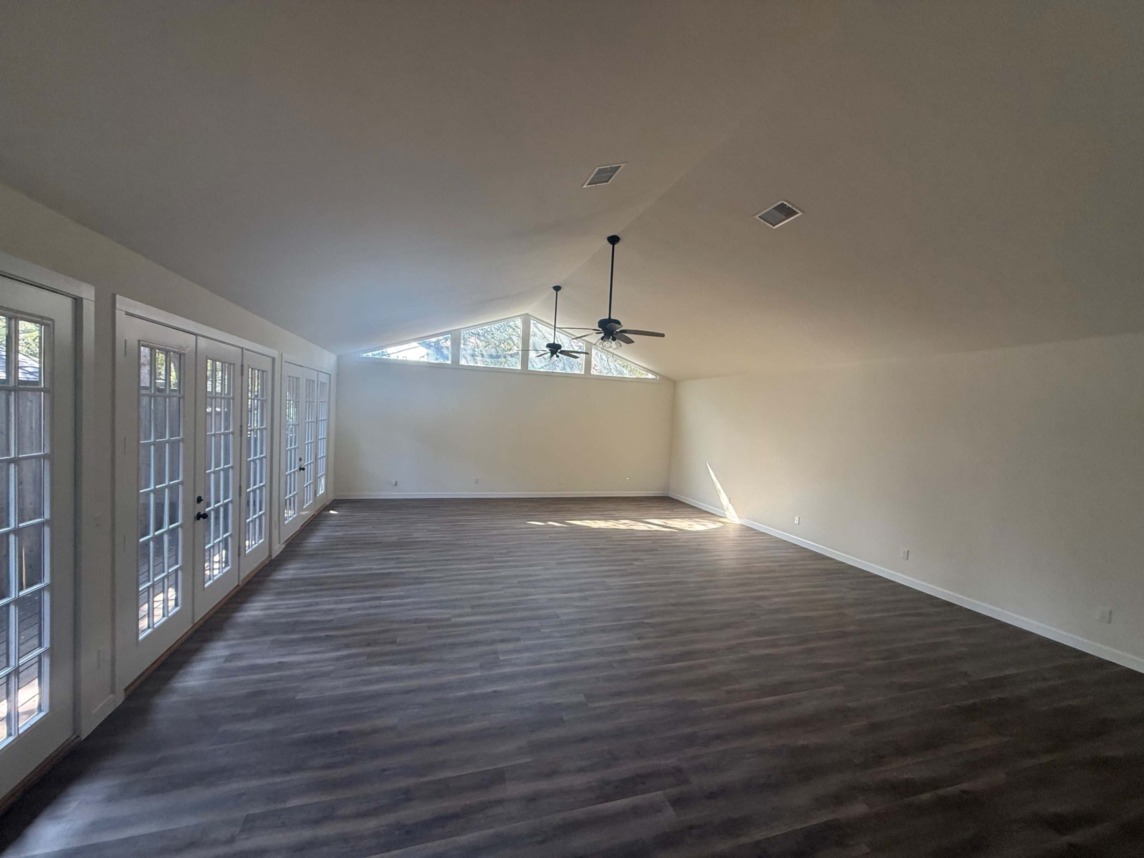 The image shows a spacious, empty room with light-colored walls, a high ceiling, and large windows along one side.