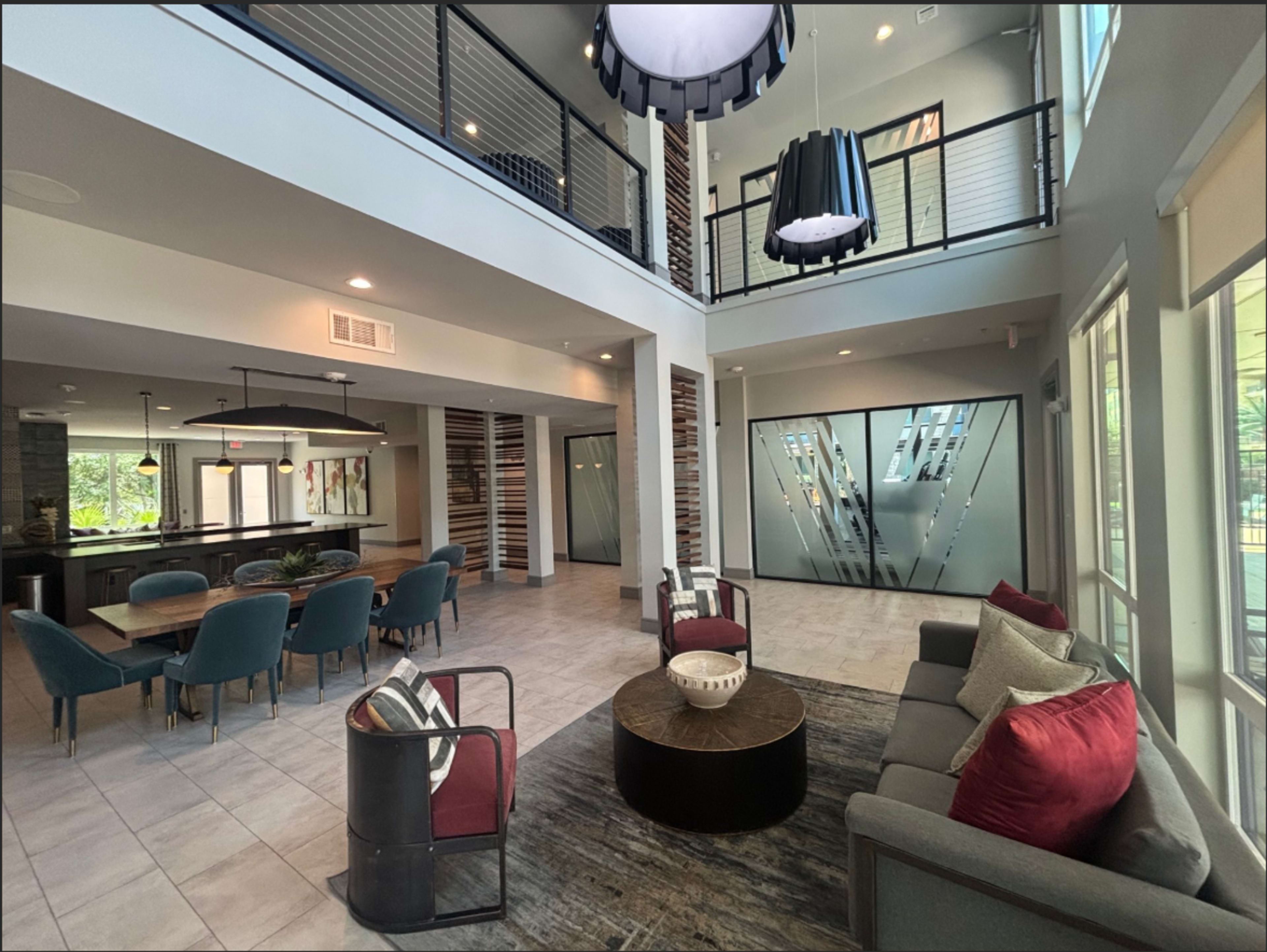 The image shows a modern, open-concept common area with a seating arrangement, dining table, and two large pendant lights hanging from the ceiling.