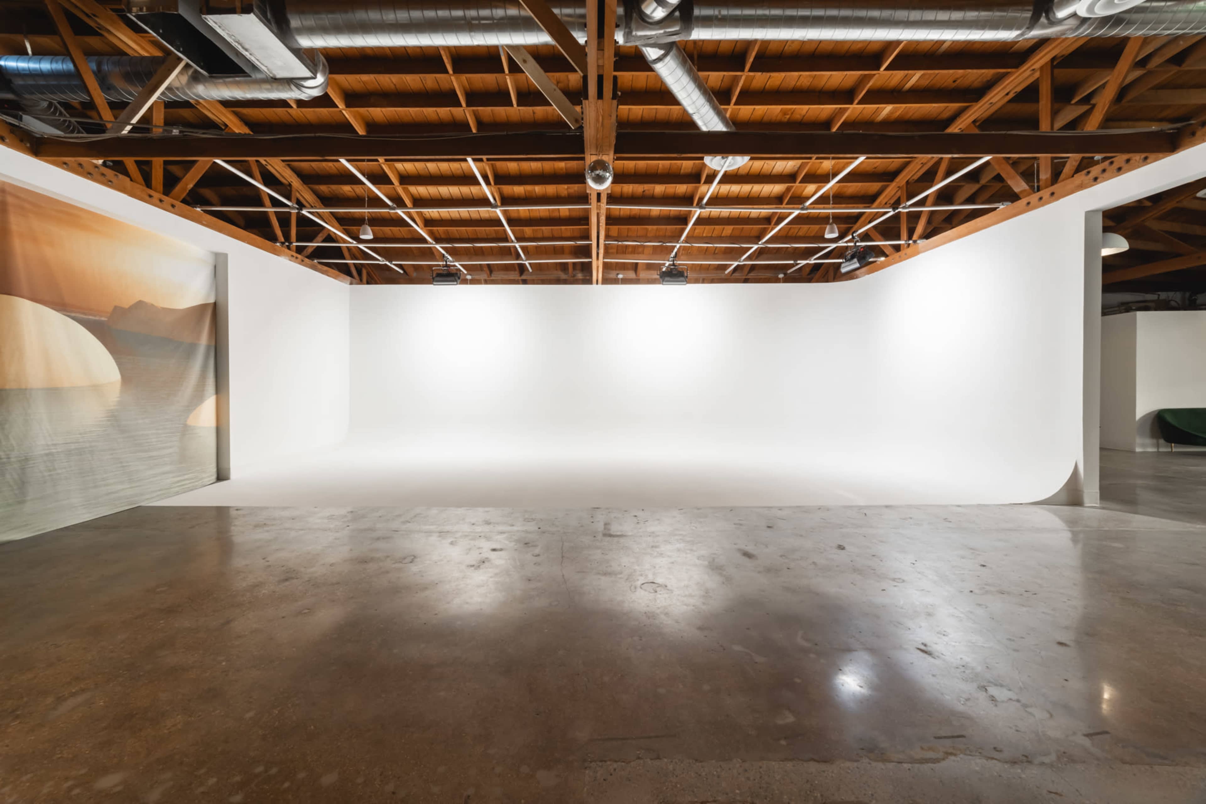 A spacious, empty art studio with a seamless white backdrop and polished concrete floor.