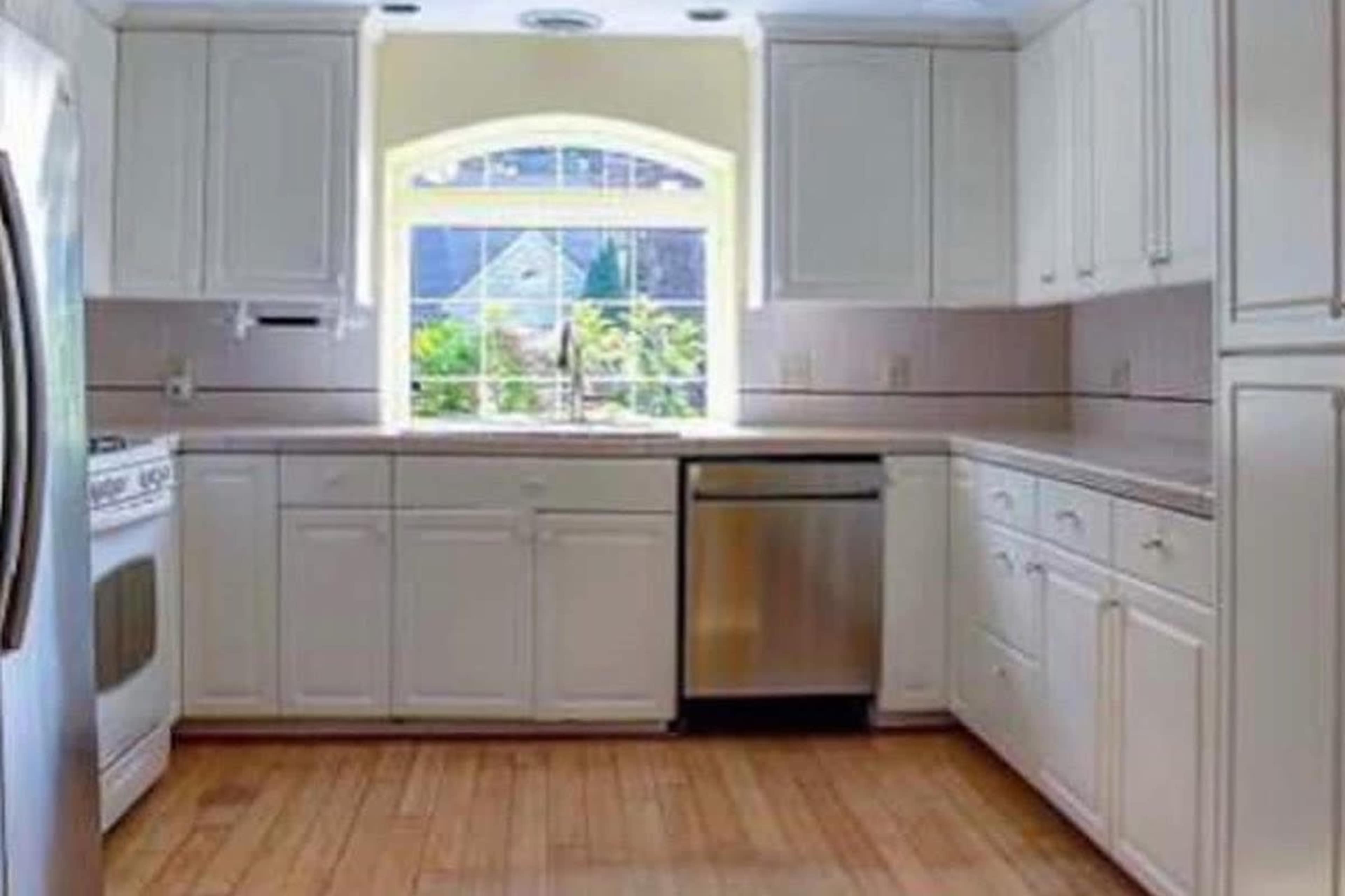 A modern kitchen with white cabinets, stainless steel appliances, and a window overlooking a garden.