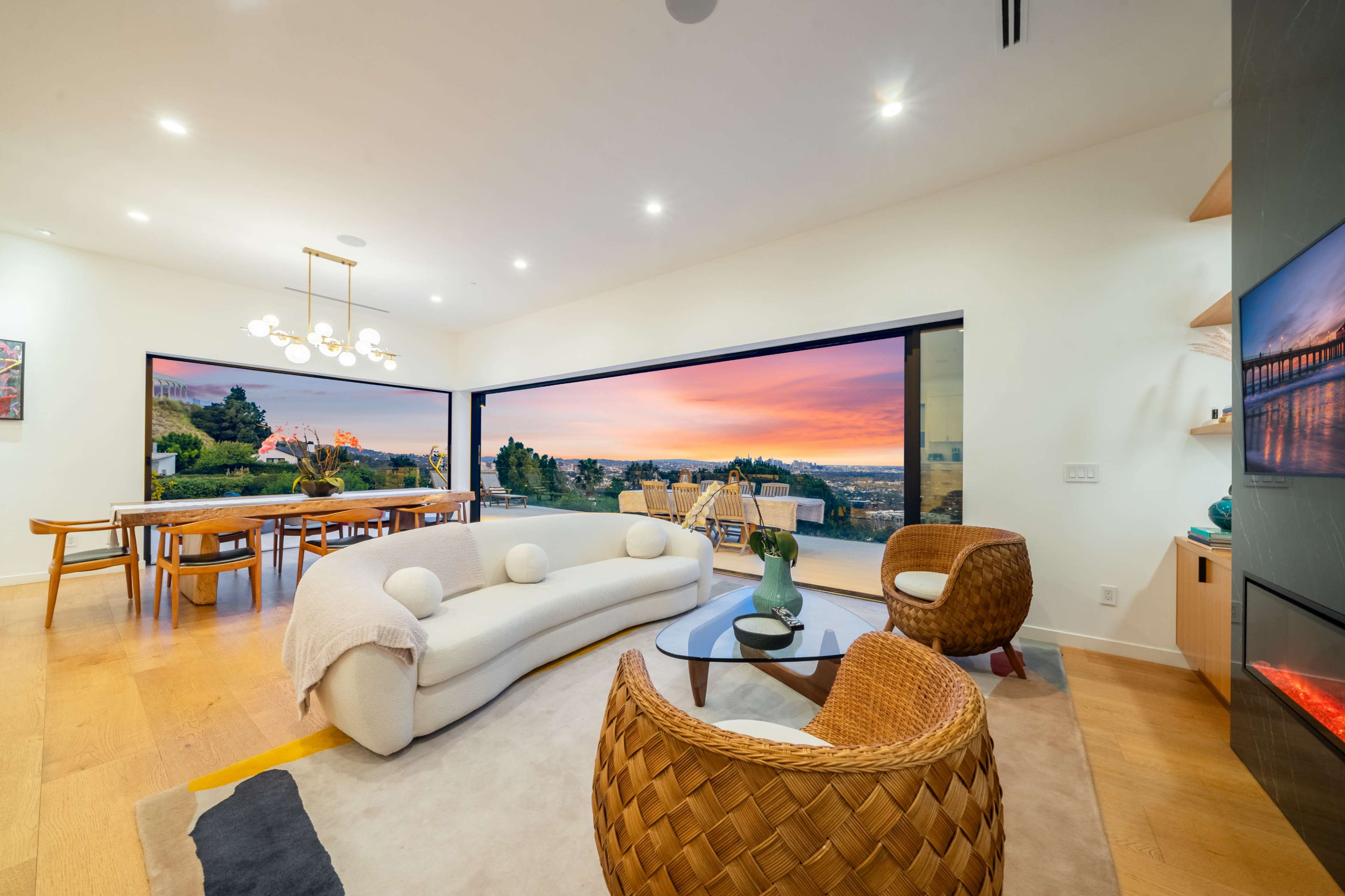 The living room features a spacious layout with modern furniture and large windows showcasing a colorful sunset view.
