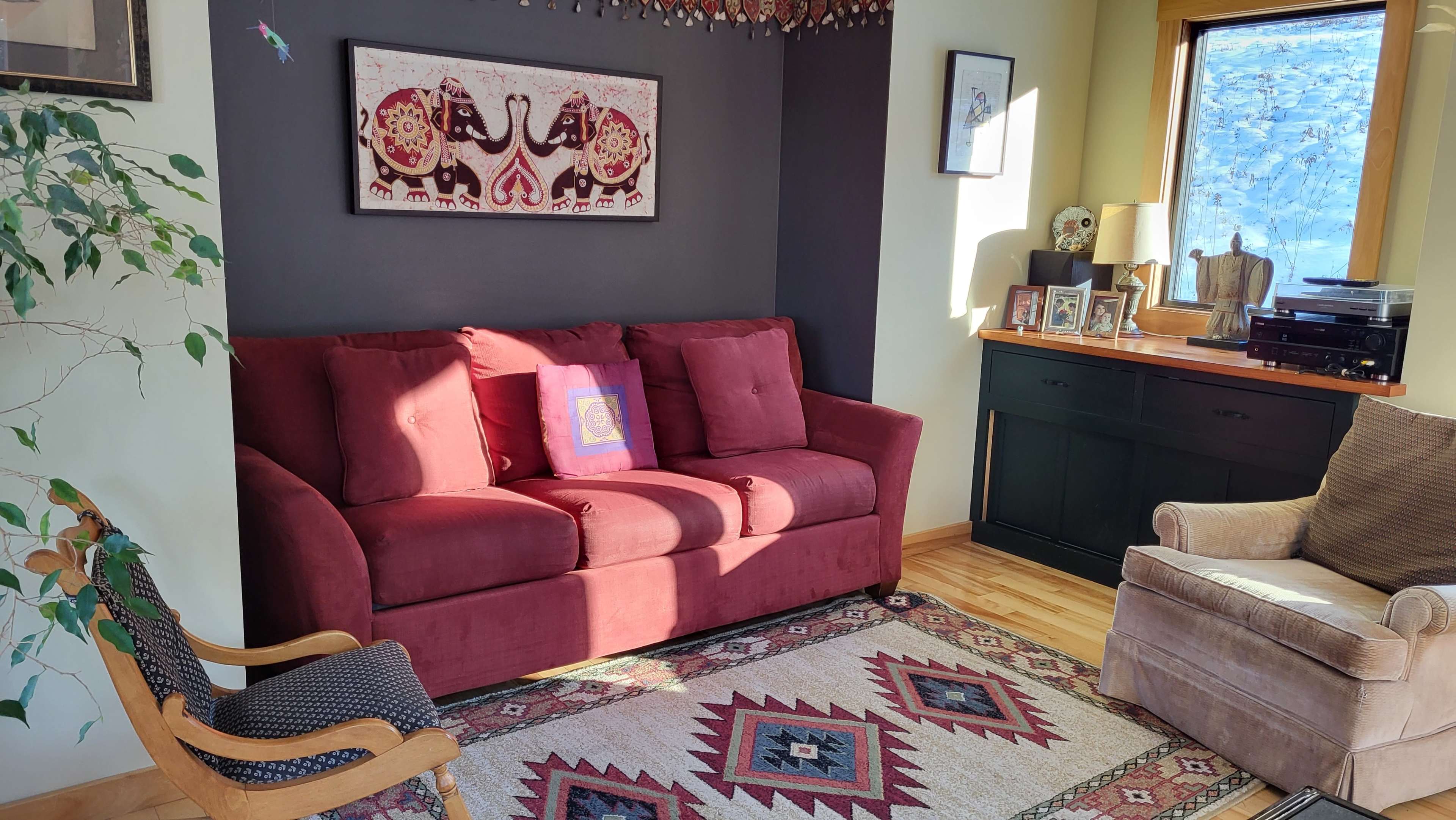The living room features a red sofa, a patterned area rug, and wooden furniture arranged near a window.