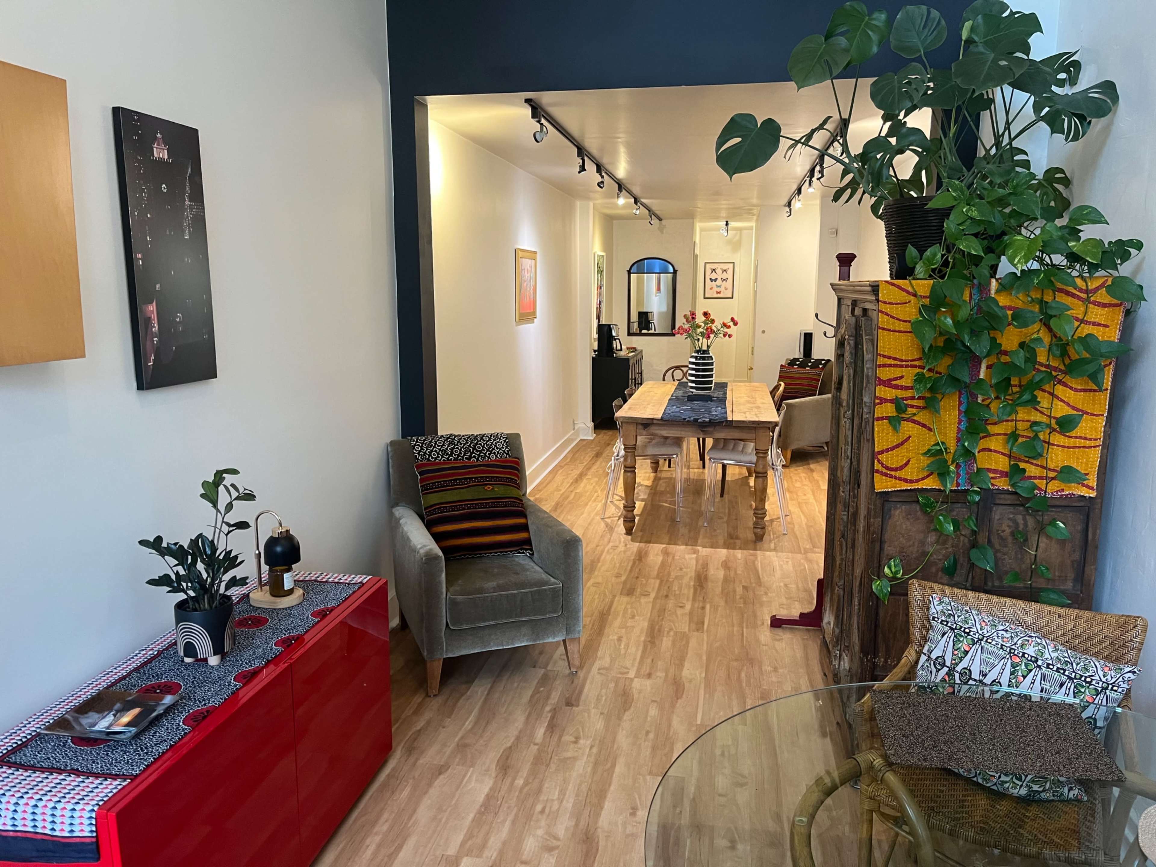The image shows an inviting hallway leading to a dining area, adorned with plants, furniture, and artwork.