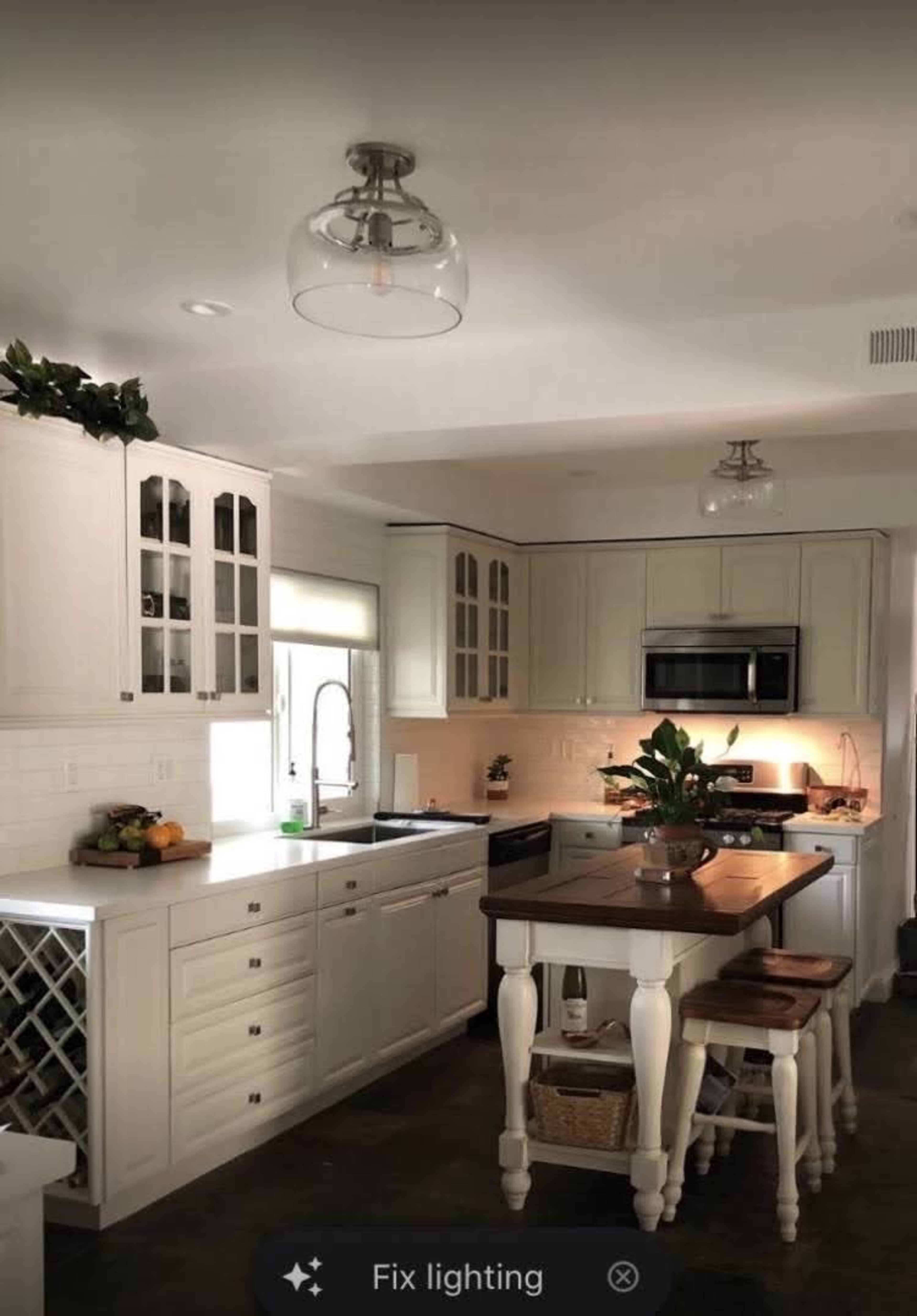 A modern kitchen features white cabinetry, a central island with bar stools, and stainless steel appliances.