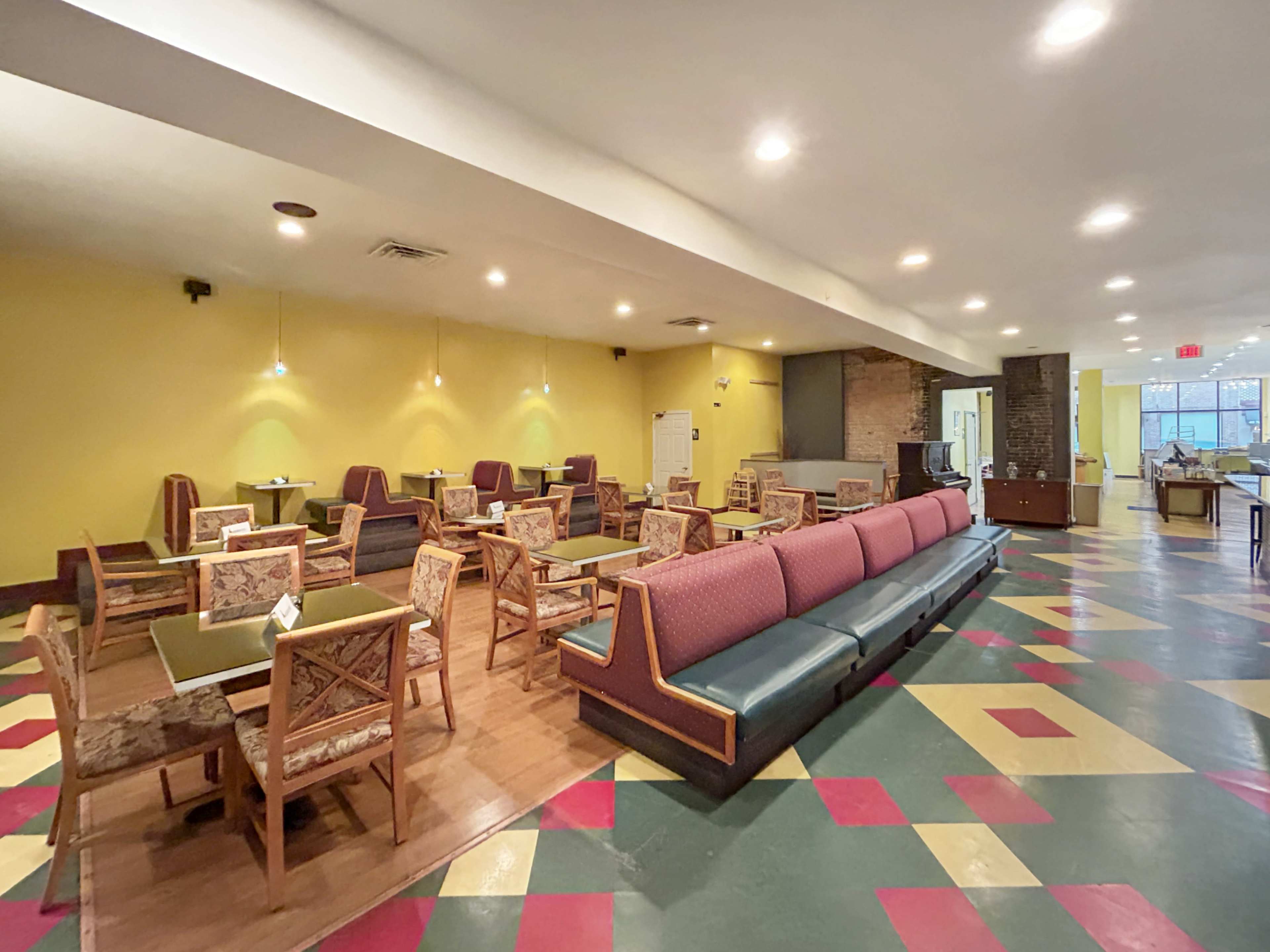 A spacious dining area with patterned flooring, several tables and chairs, and a brightly colored yellow wall.