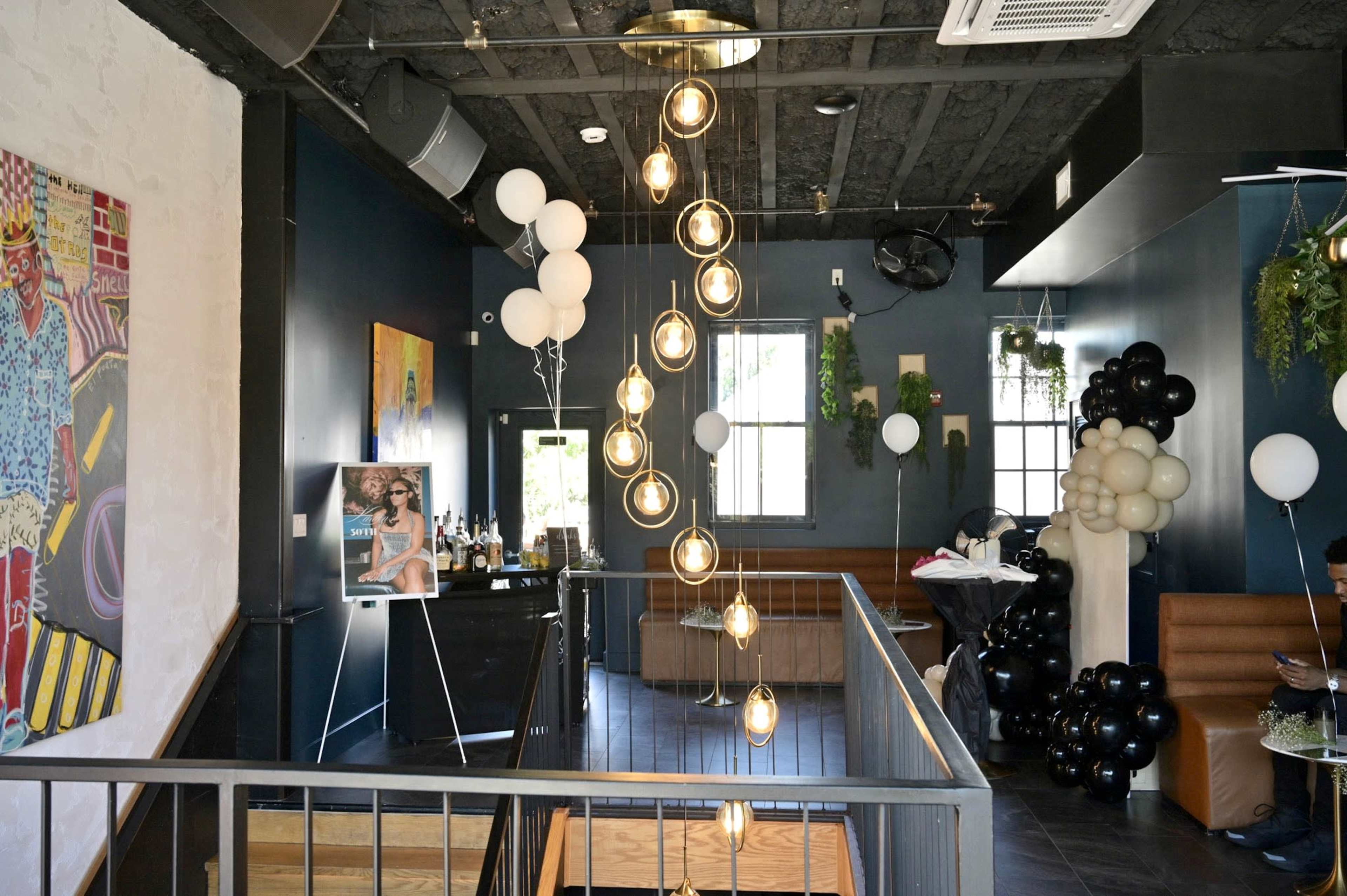 The image shows an interior view of a trendy restaurant or lounge with stylish lighting, modern decor, and a mix of seating areas.