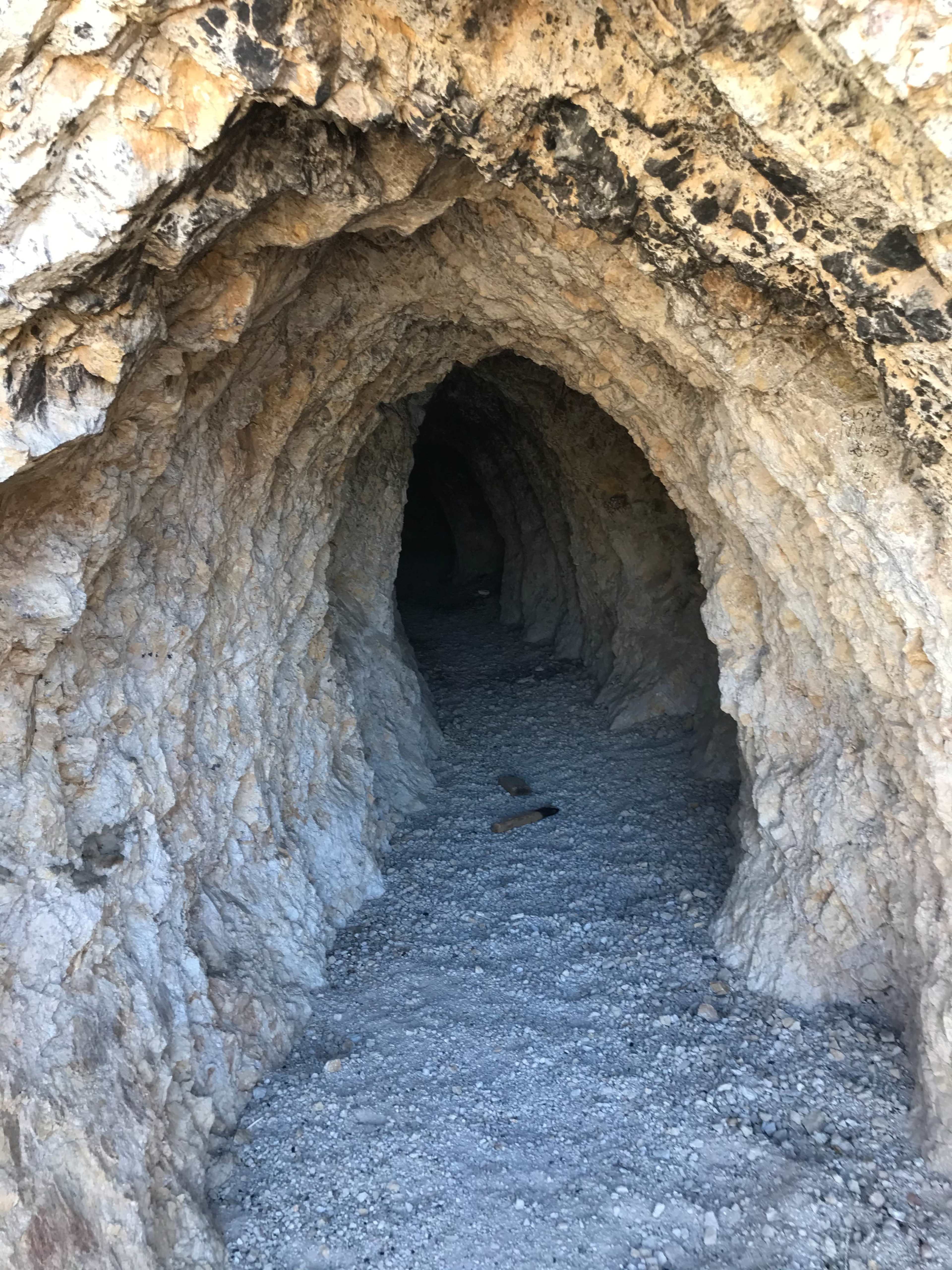 The entrance of a rocky cave with a gravelly path leading into darkness.