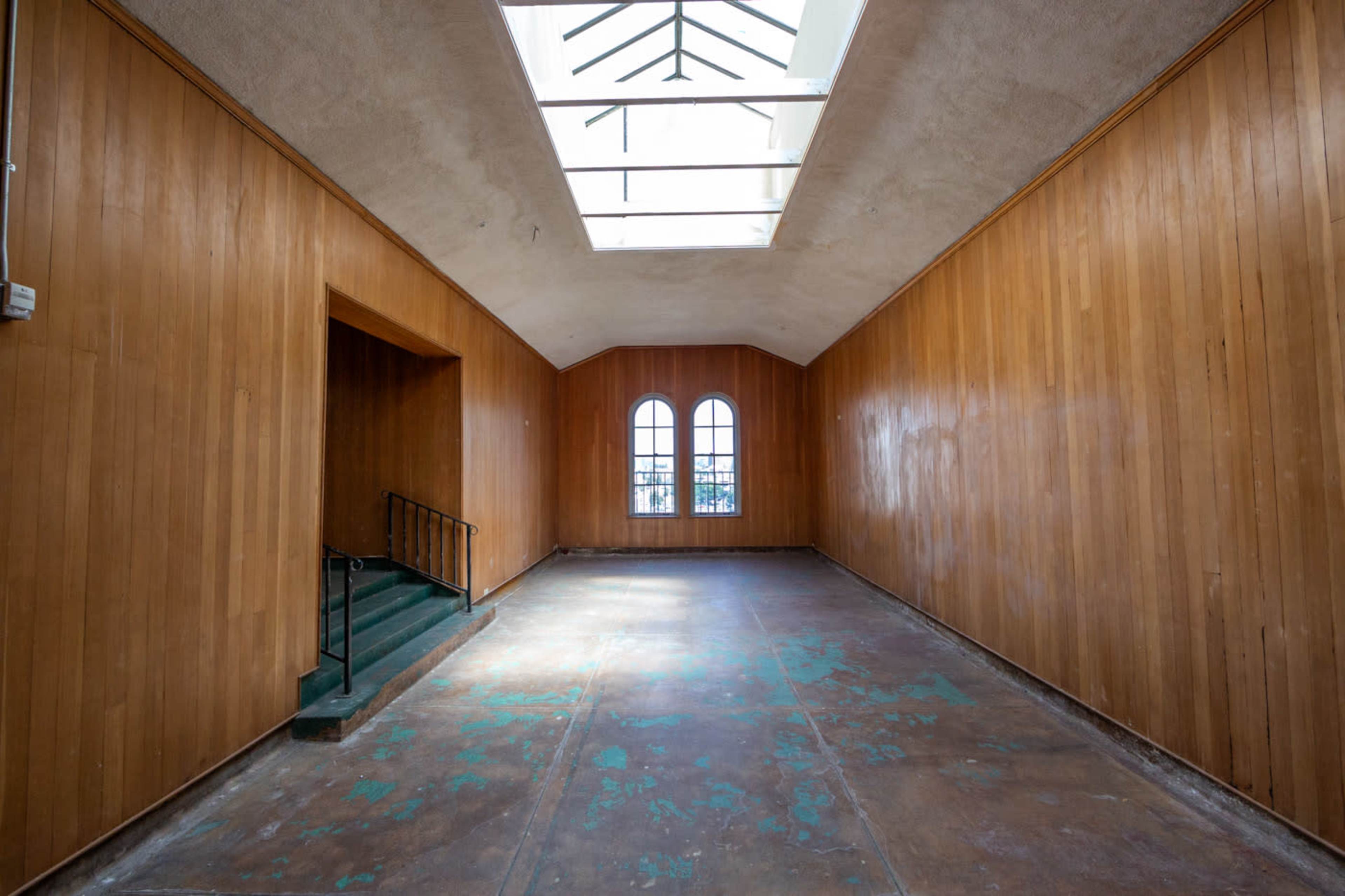 The image shows a spacious, empty interior room with wooden paneled walls, a skylight overhead, and a staircase leading to a lower level.