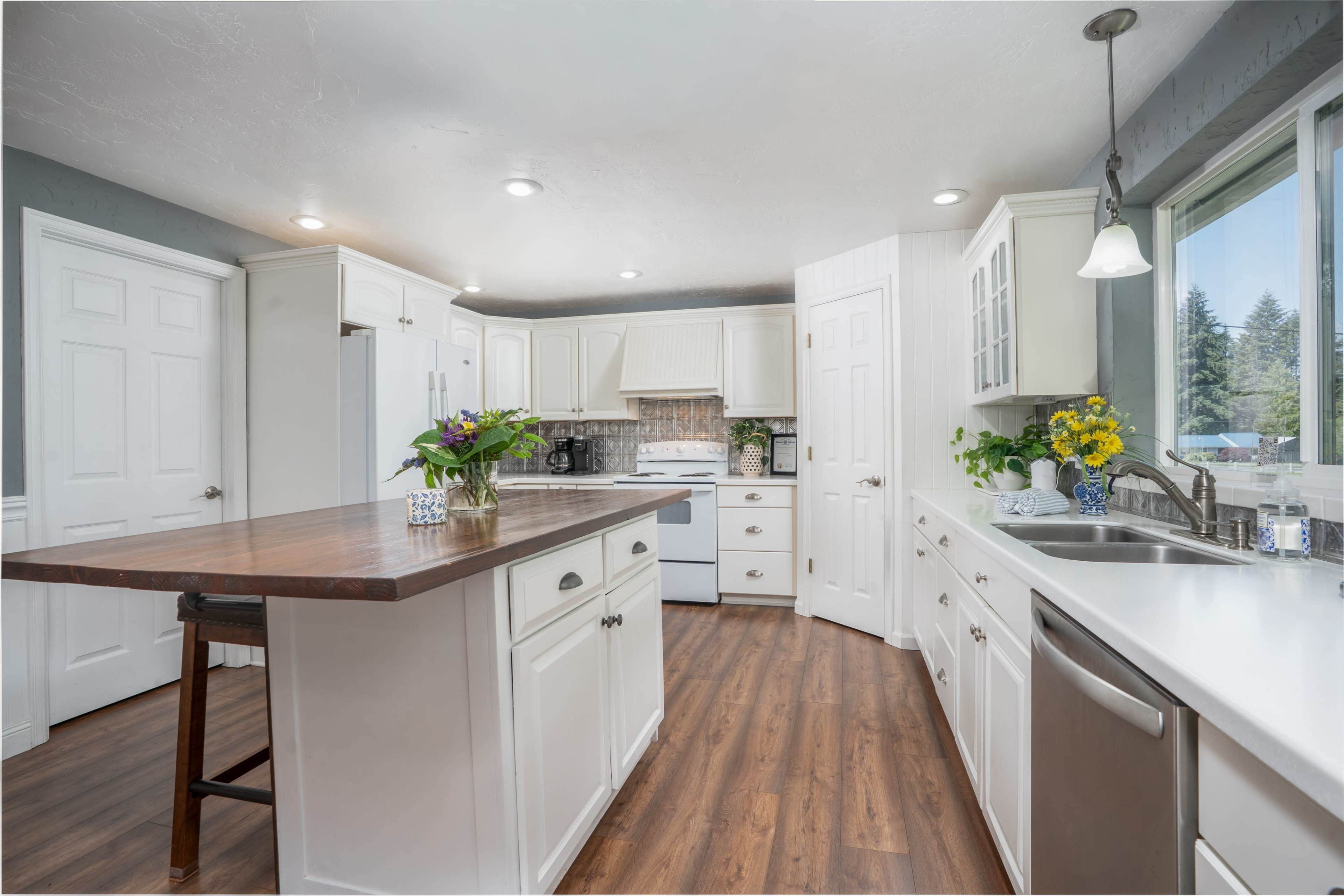 The image shows a bright kitchen with white cabinetry, a large wooden island, and modern appliances.