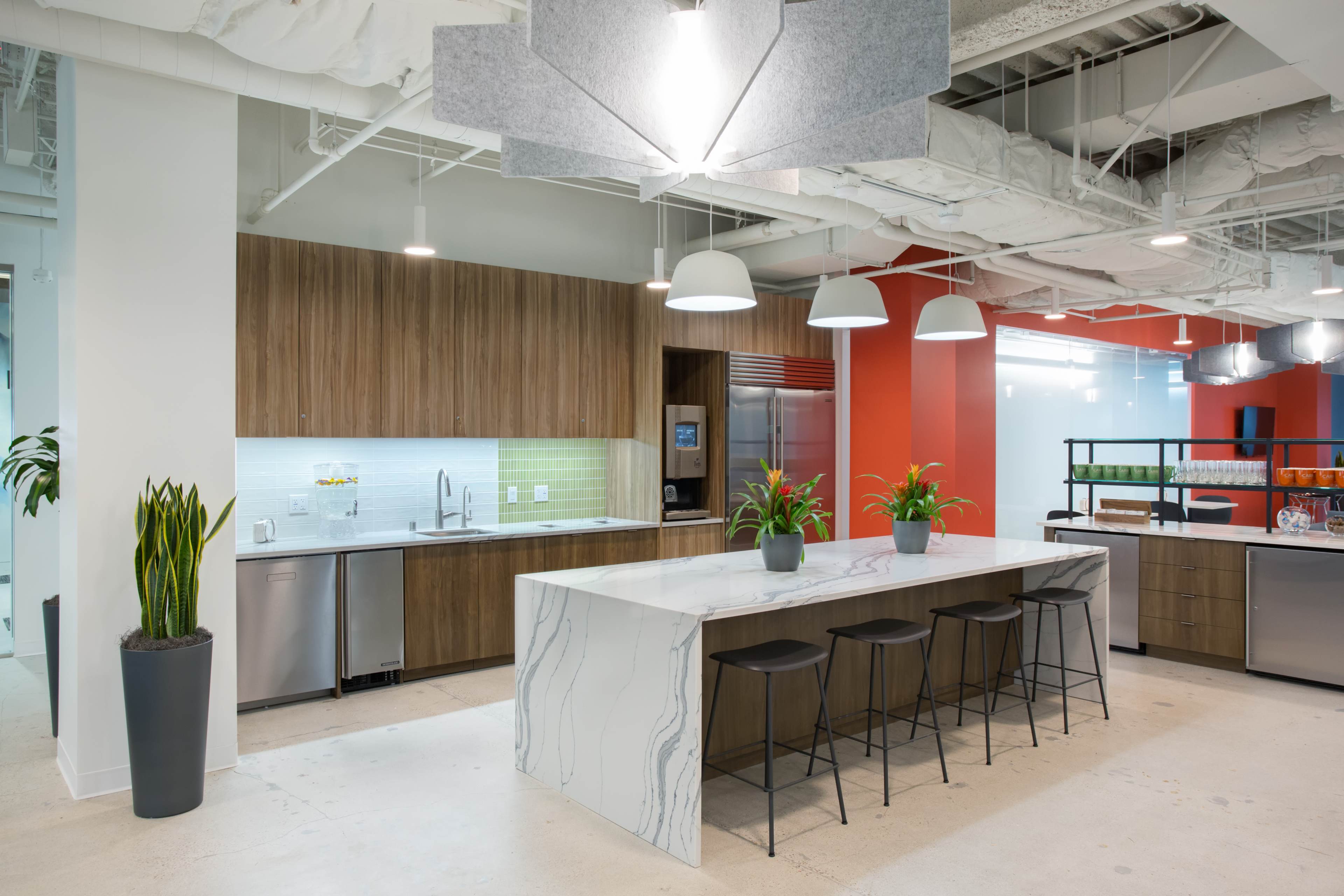 A modern kitchen area in an office with wooden cabinetry, a marble countertop island, and pendant lighting.