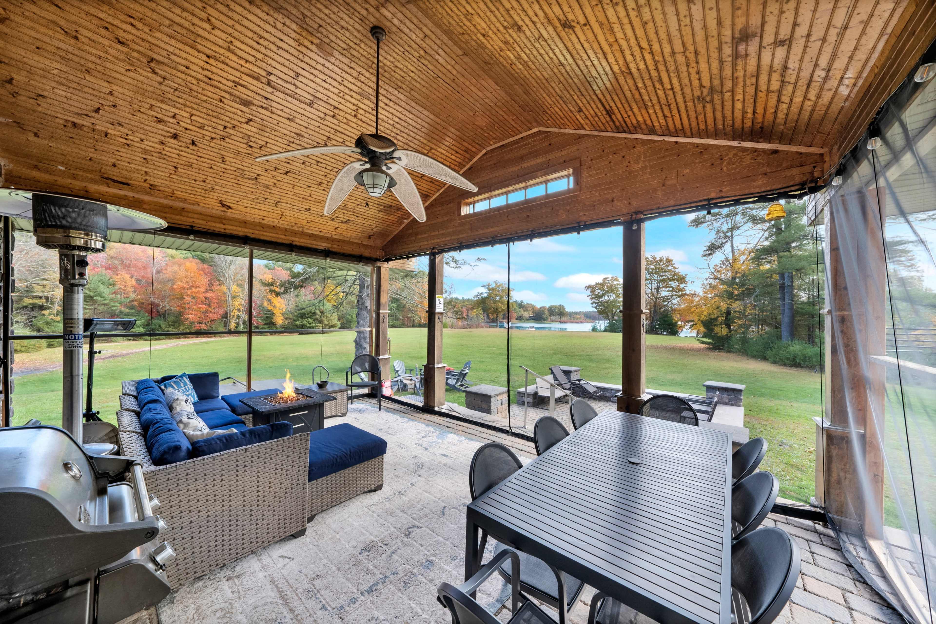 A screened porch with a dining table and seating area overlooking a green yard surrounded by trees.