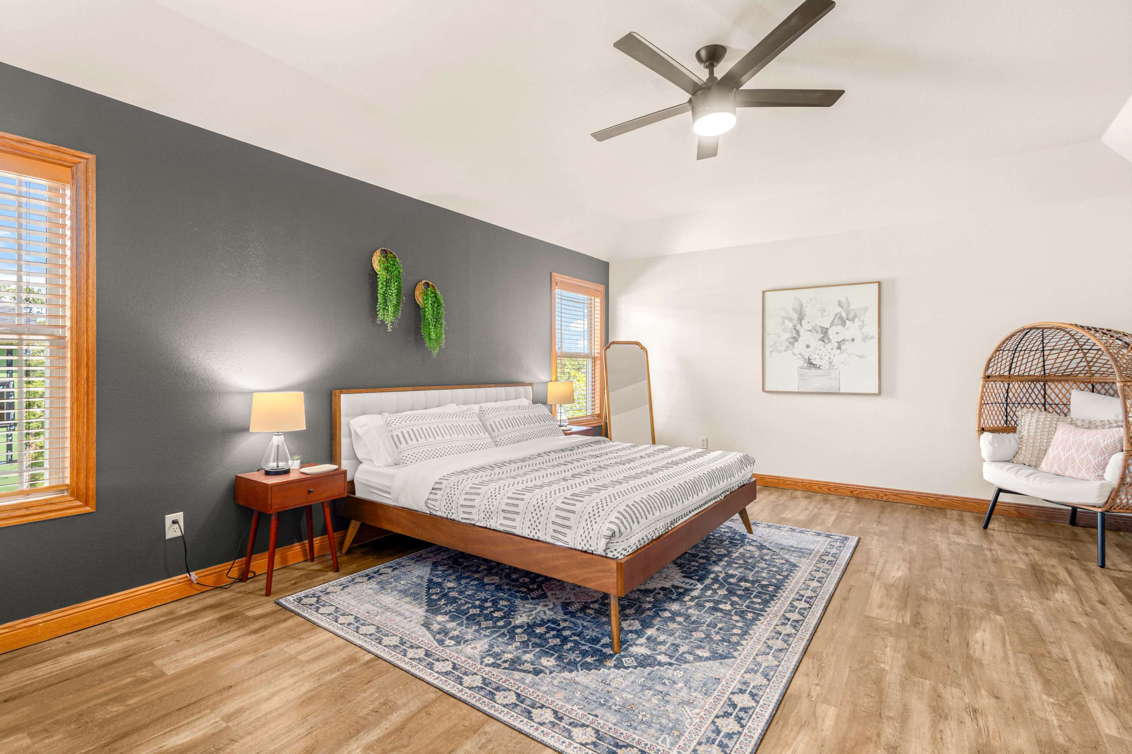 The image shows a stylish bedroom with a bed, a decorative wall, large windows, and a chair in a cozy corner.