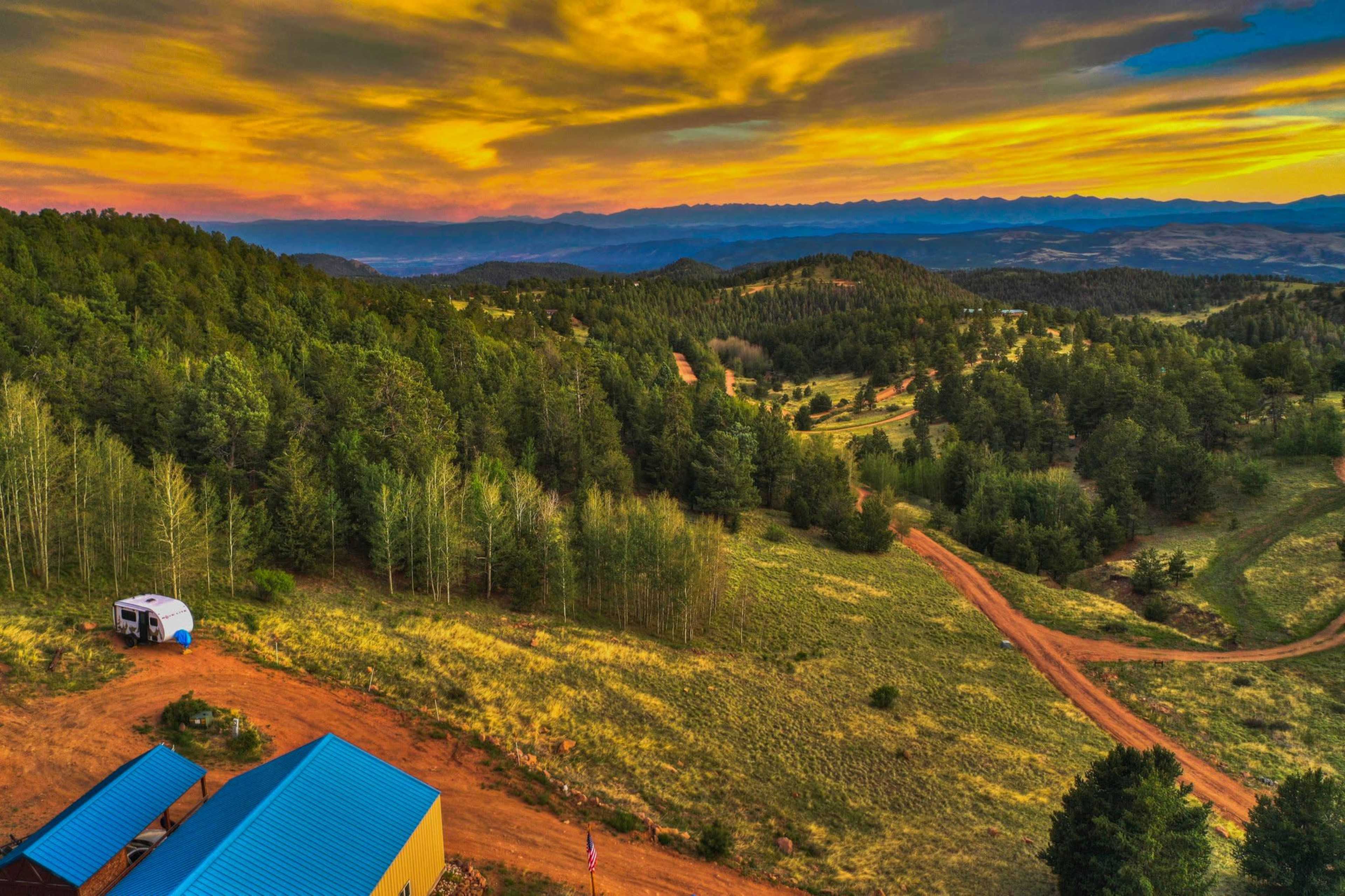 A scenic landscape with rolling hills, a dirt road winding through green forested areas, and a colorful sunset sky.