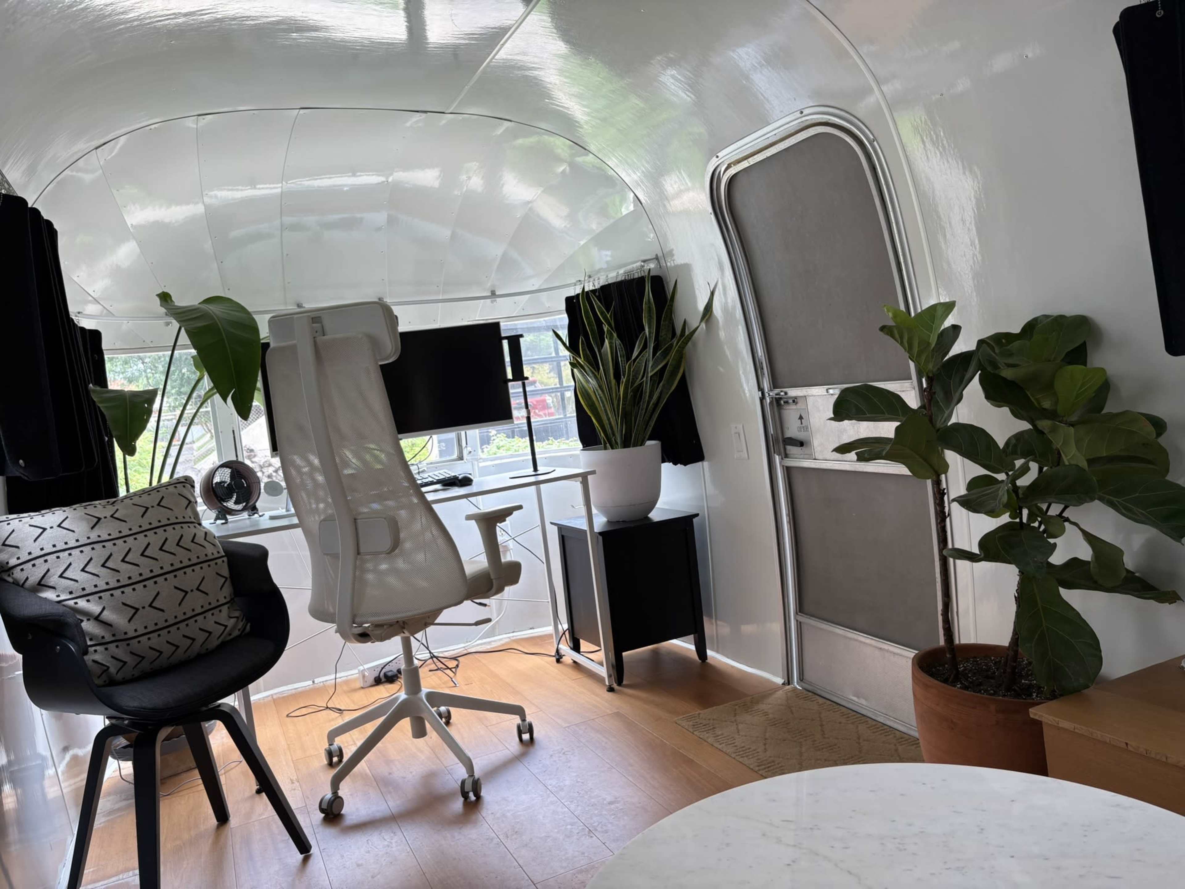 The interior of a modern, brightly lit space features an office setup with a desk, chair, and plants.