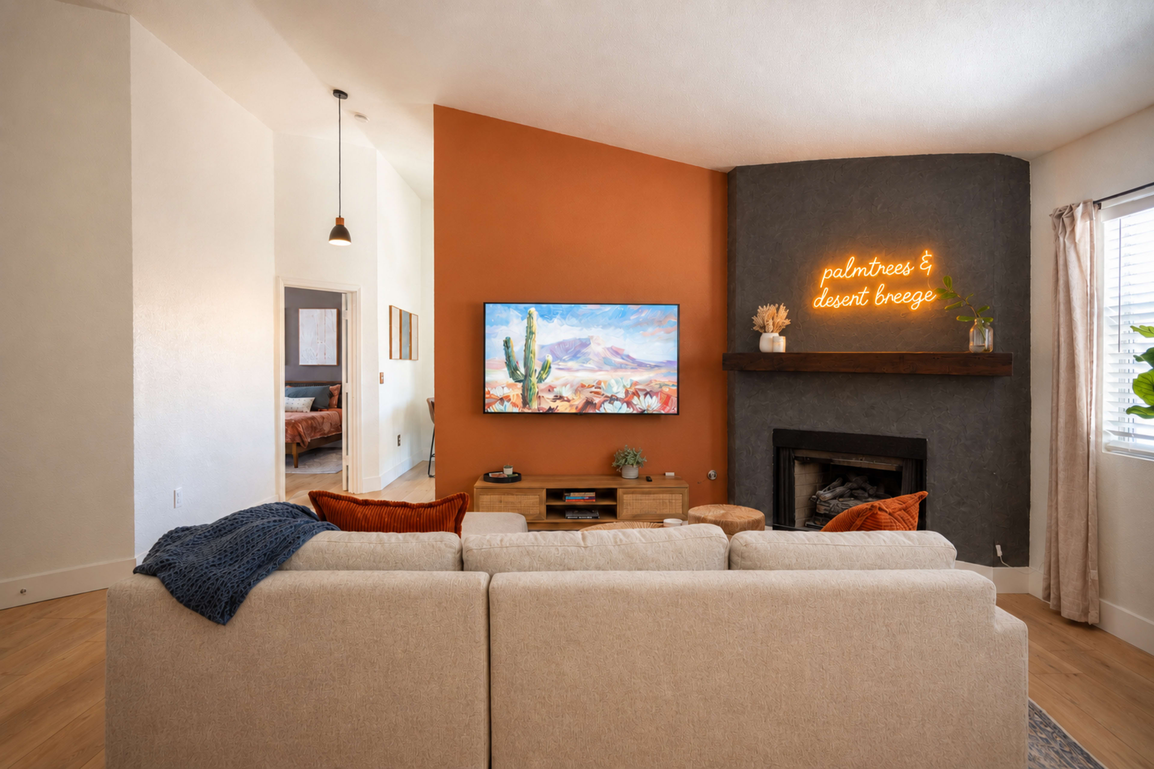 A cozy living room features a large TV mounted on a two-tone wall, a modern fireplace, and a sectional sofa with decorative pillows.