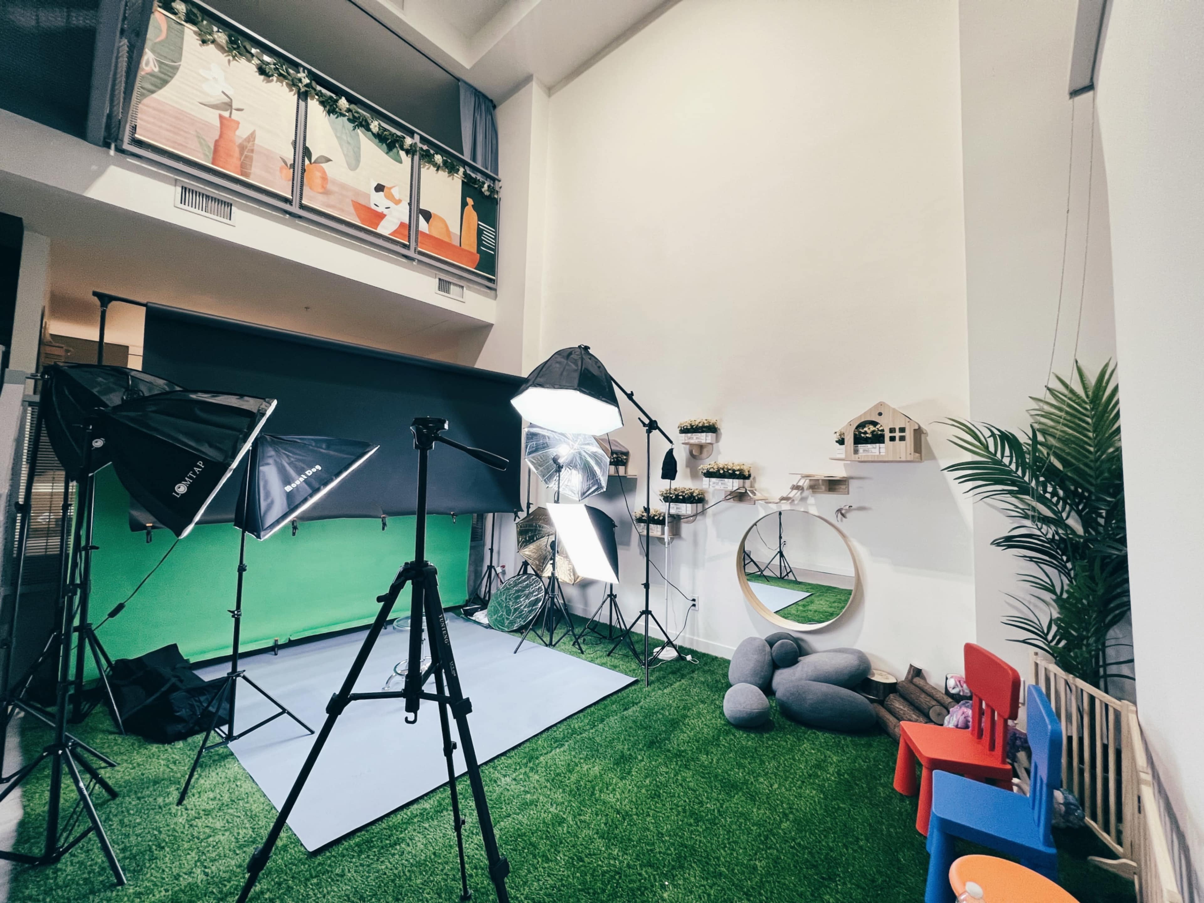 A photography studio setup with lighting equipment, a green screen backdrop, and a small play area with chairs and decorative items.