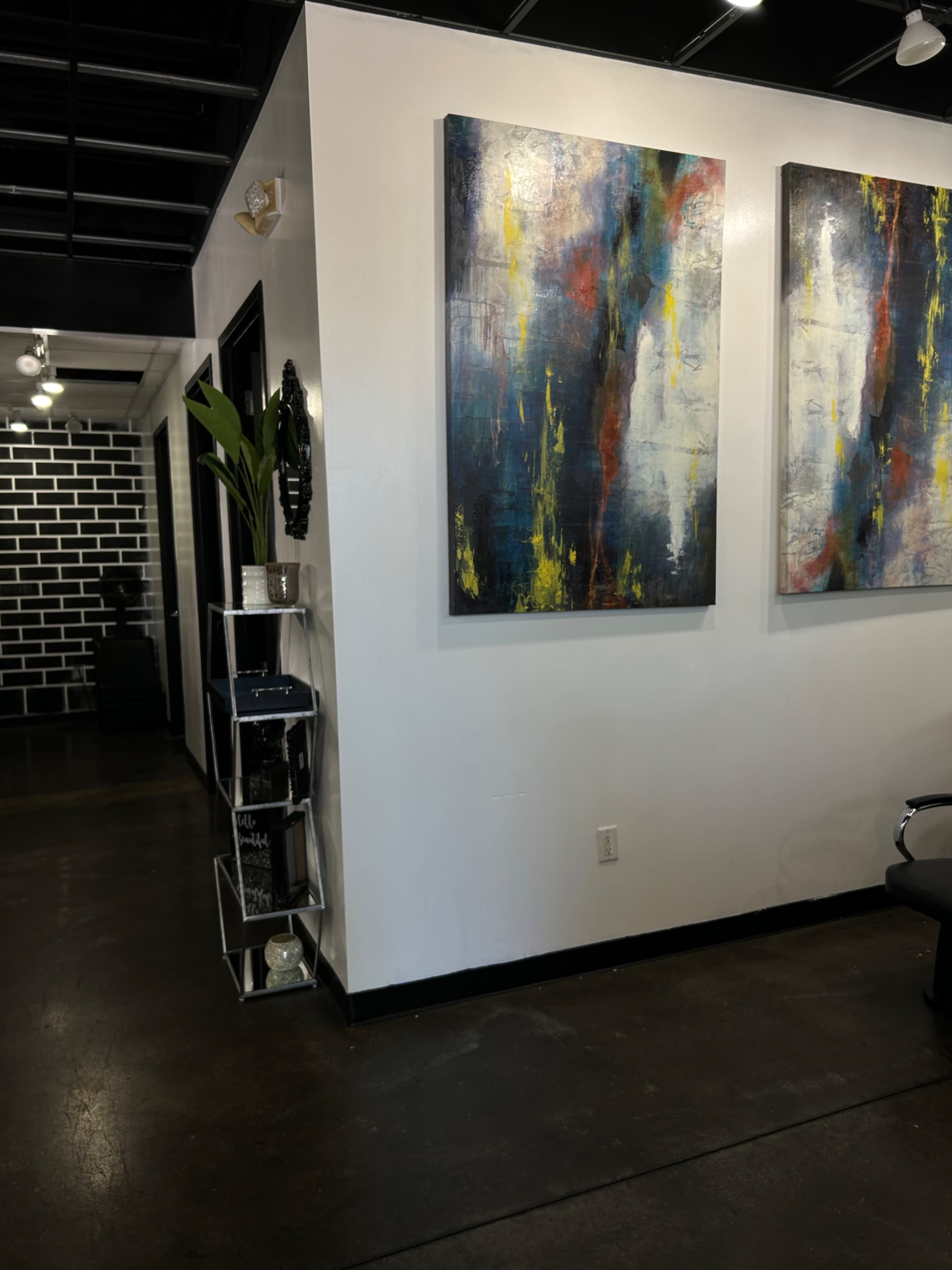 A modern interior space featuring two large abstract paintings on a white wall, a potted plant in a corner, and a black and white brick wall in the background.