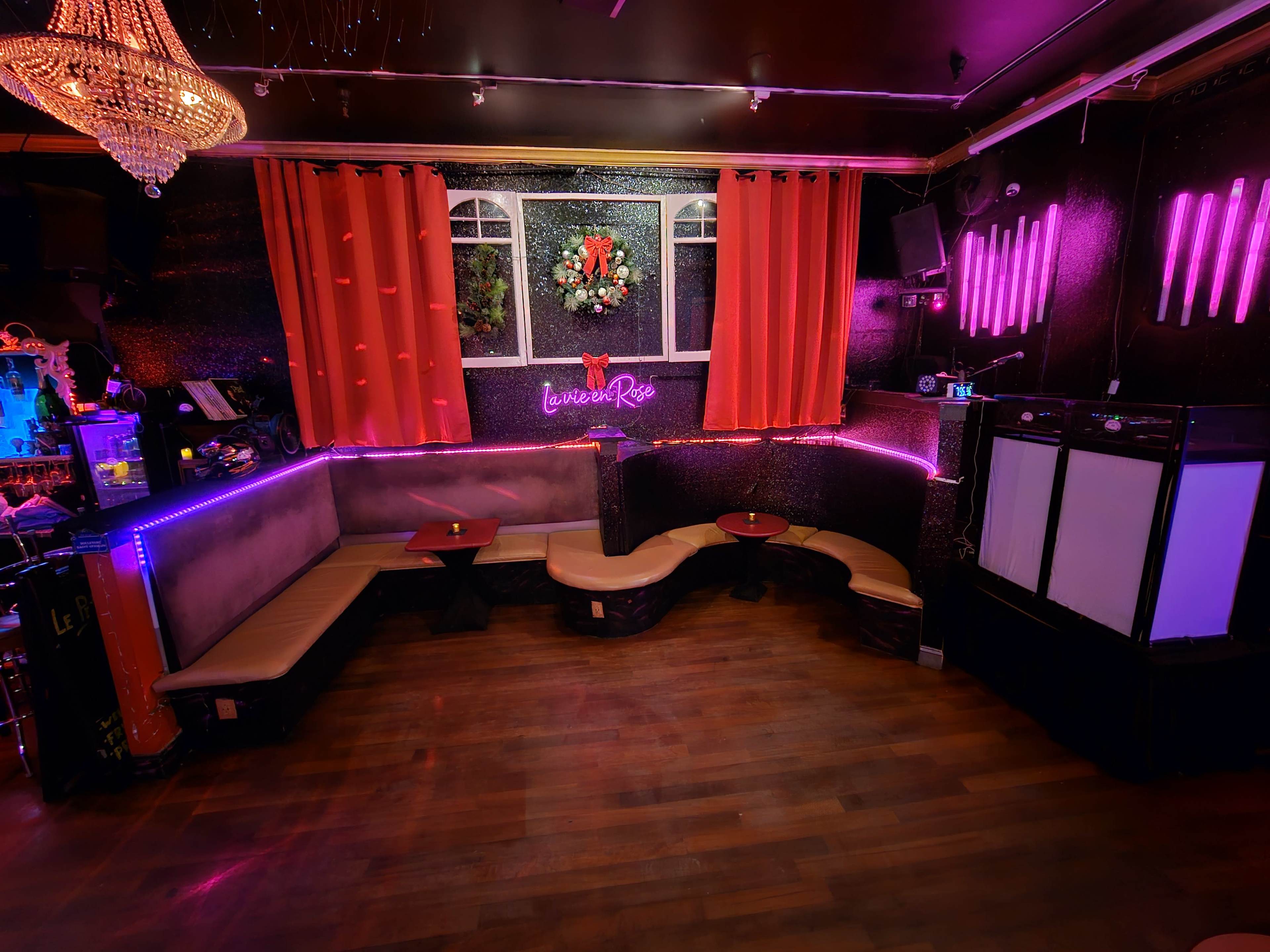 A dimly lit lounge area with curved seating, red curtains, and neon lighting against a dark wall.