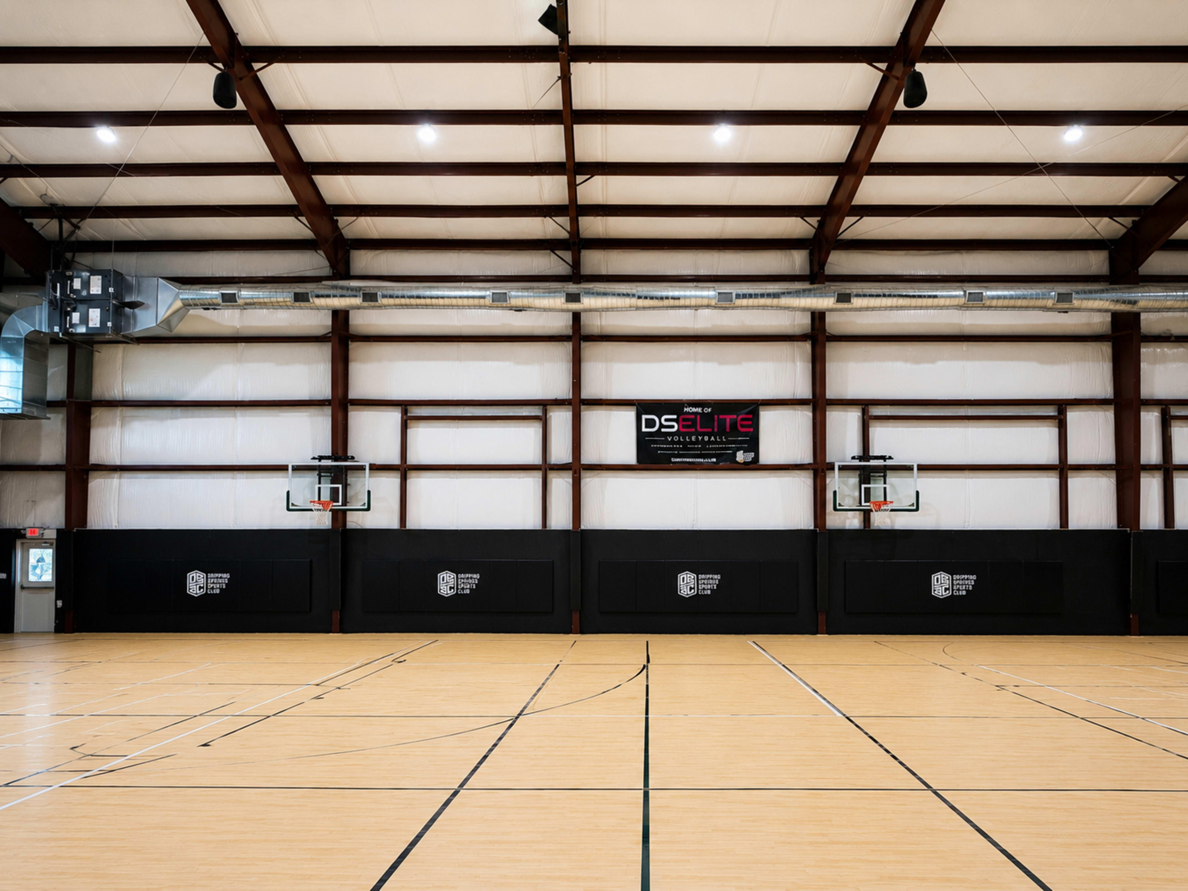 The image shows an indoor basketball court with two hoop setups on opposite ends and a large banner hanging on the wall.