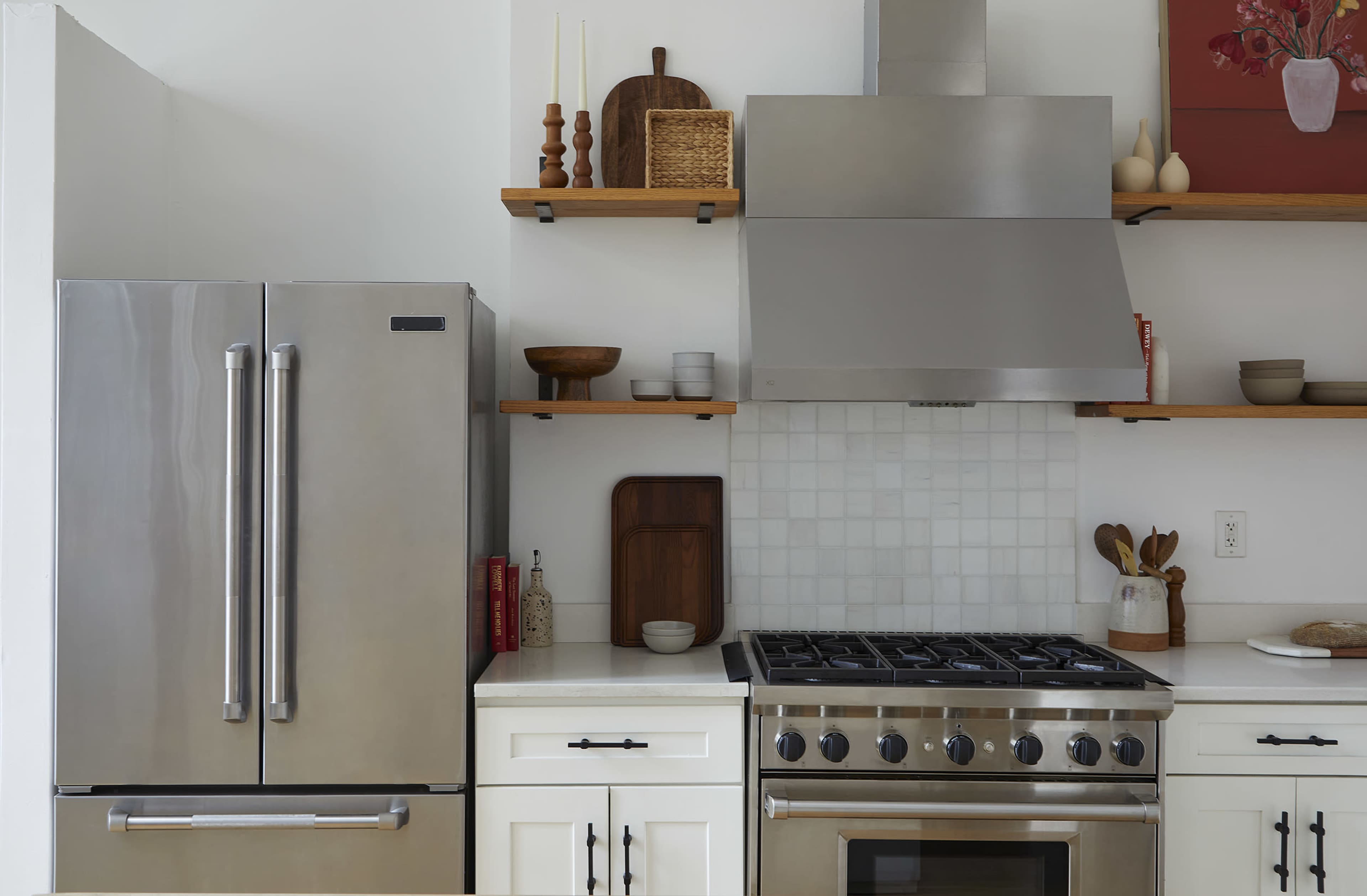 A modern kitchen features stainless steel appliances, including a refrigerator and a range, with open shelving displaying various kitchenware.