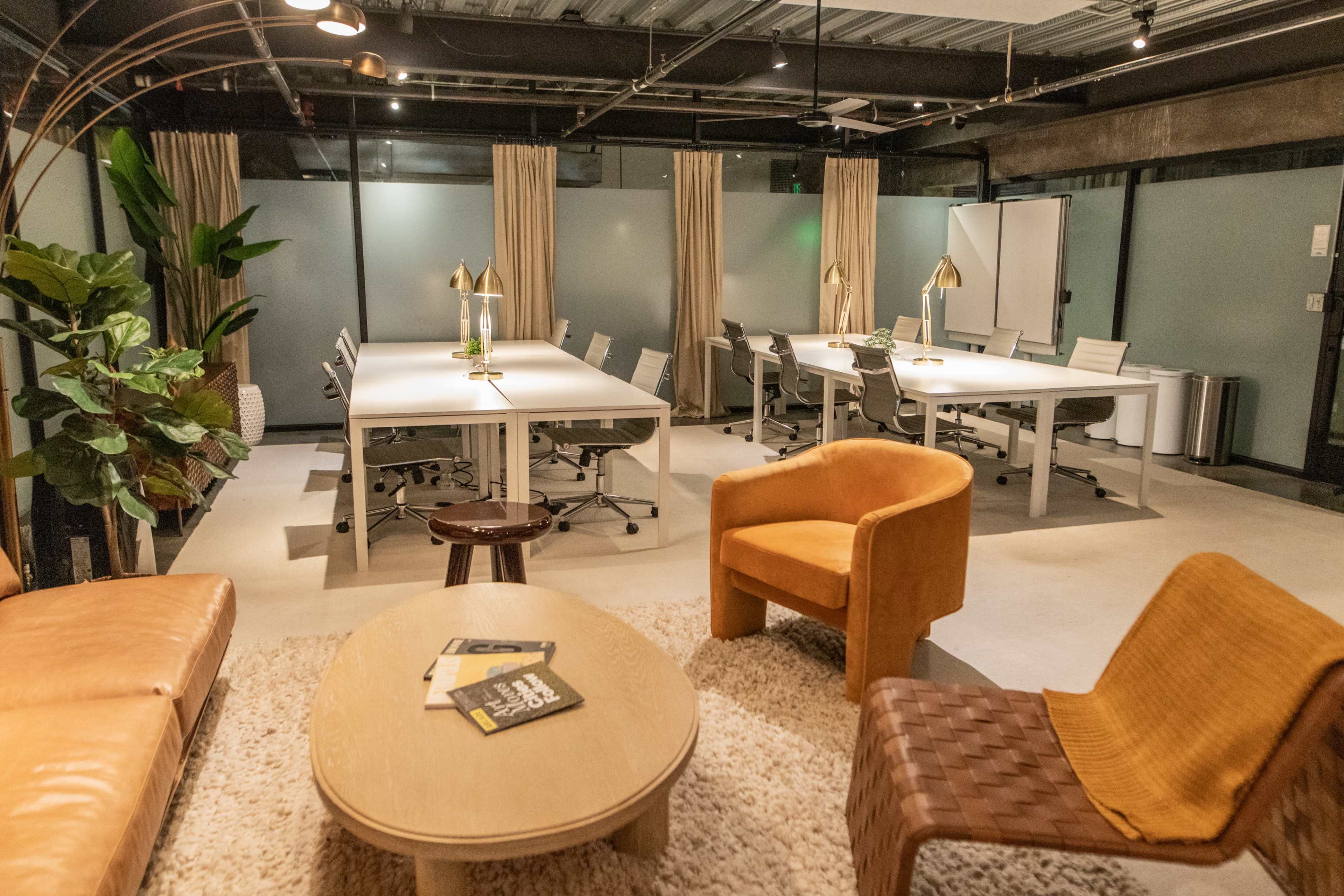 The image shows a modern office space featuring several work desks, chairs, and a seating area with a sofa and chairs.