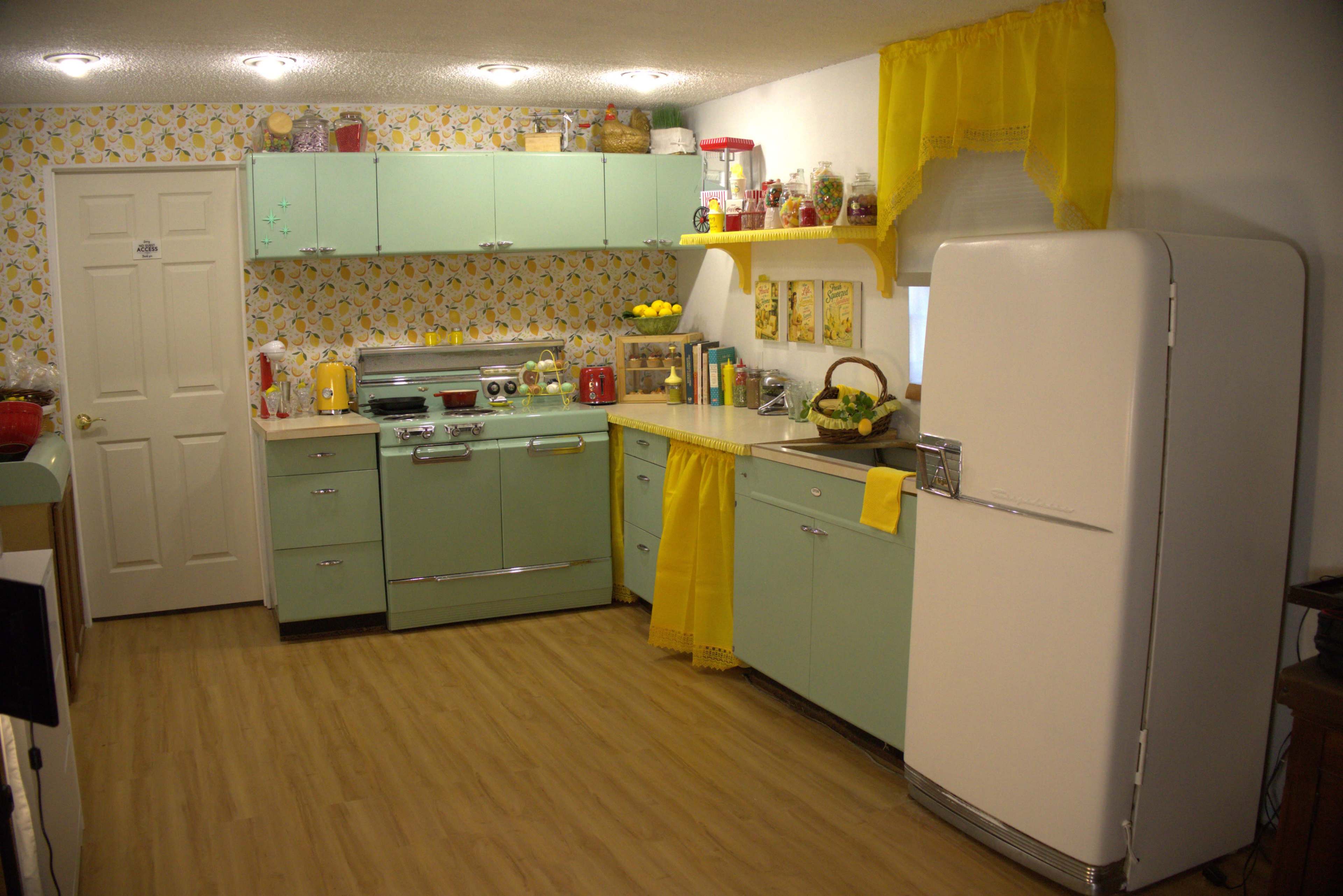 The kitchen features mint green cabinets, a vintage-style refrigerator, and yellow floral wallpaper with matching curtains.