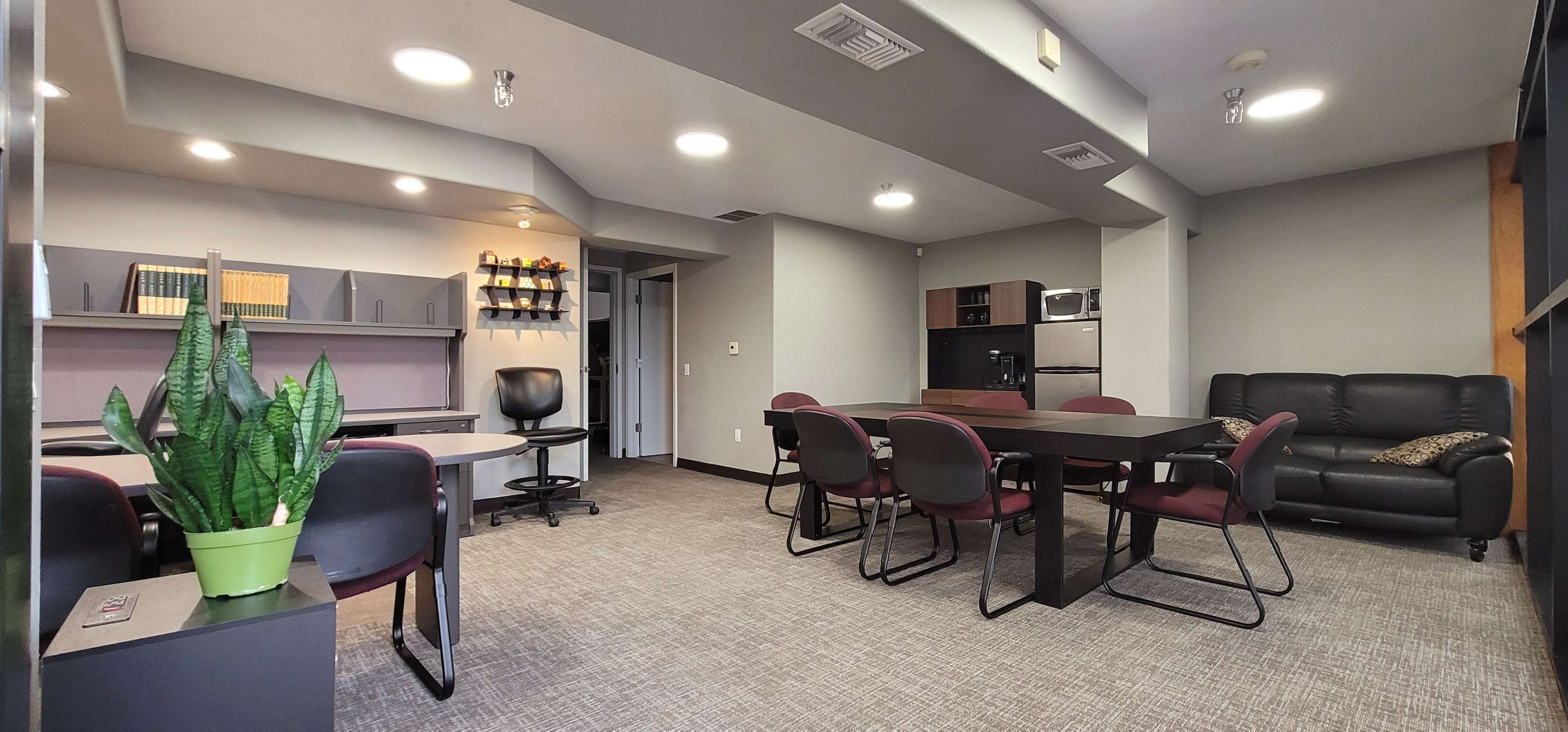 The image shows a modern office space with a seating area, a conference table, and a kitchenette in a well-lit room.