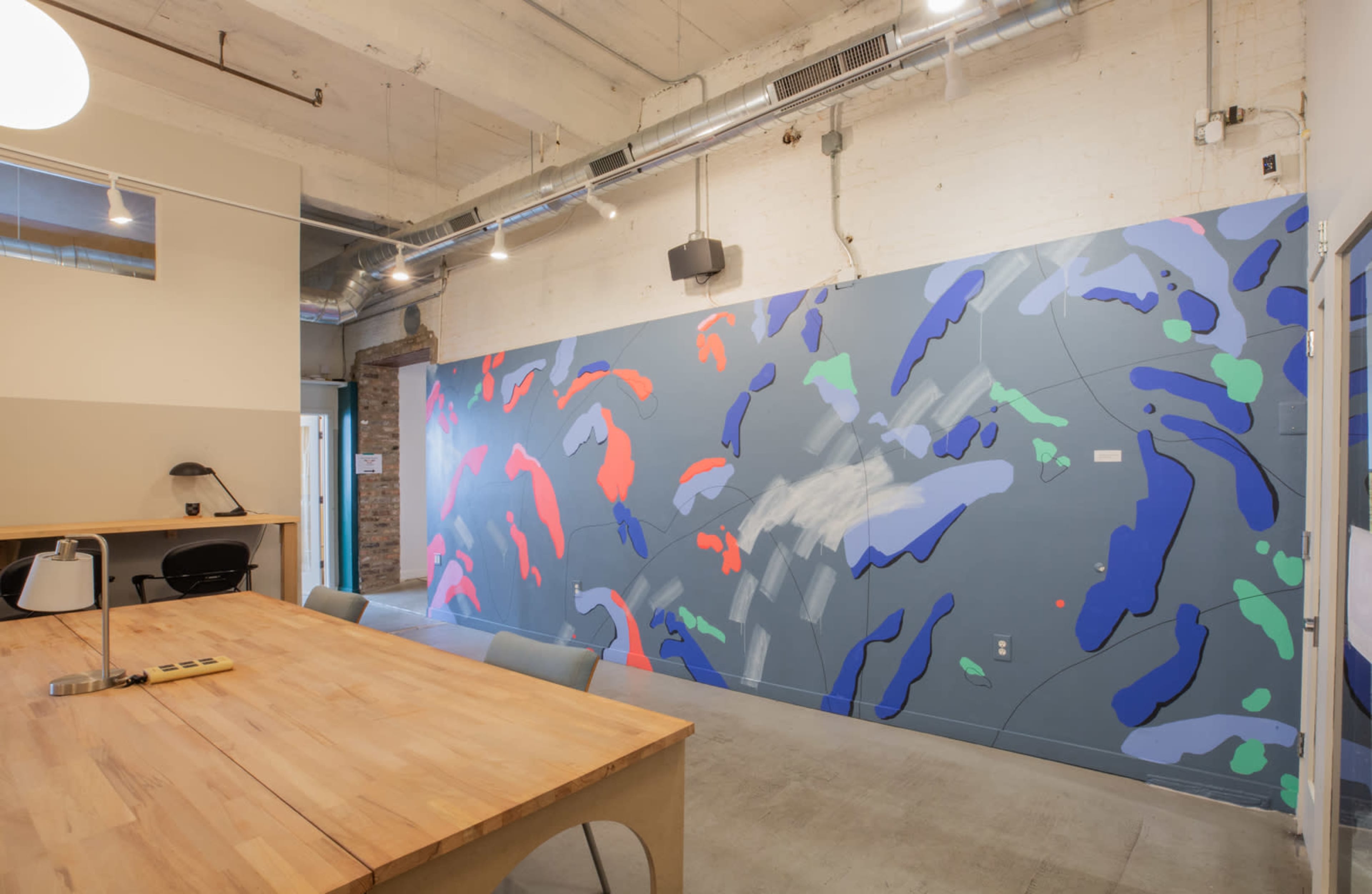 A modern office space featuring a colorful abstract mural on one wall and a wooden table with chairs nearby.