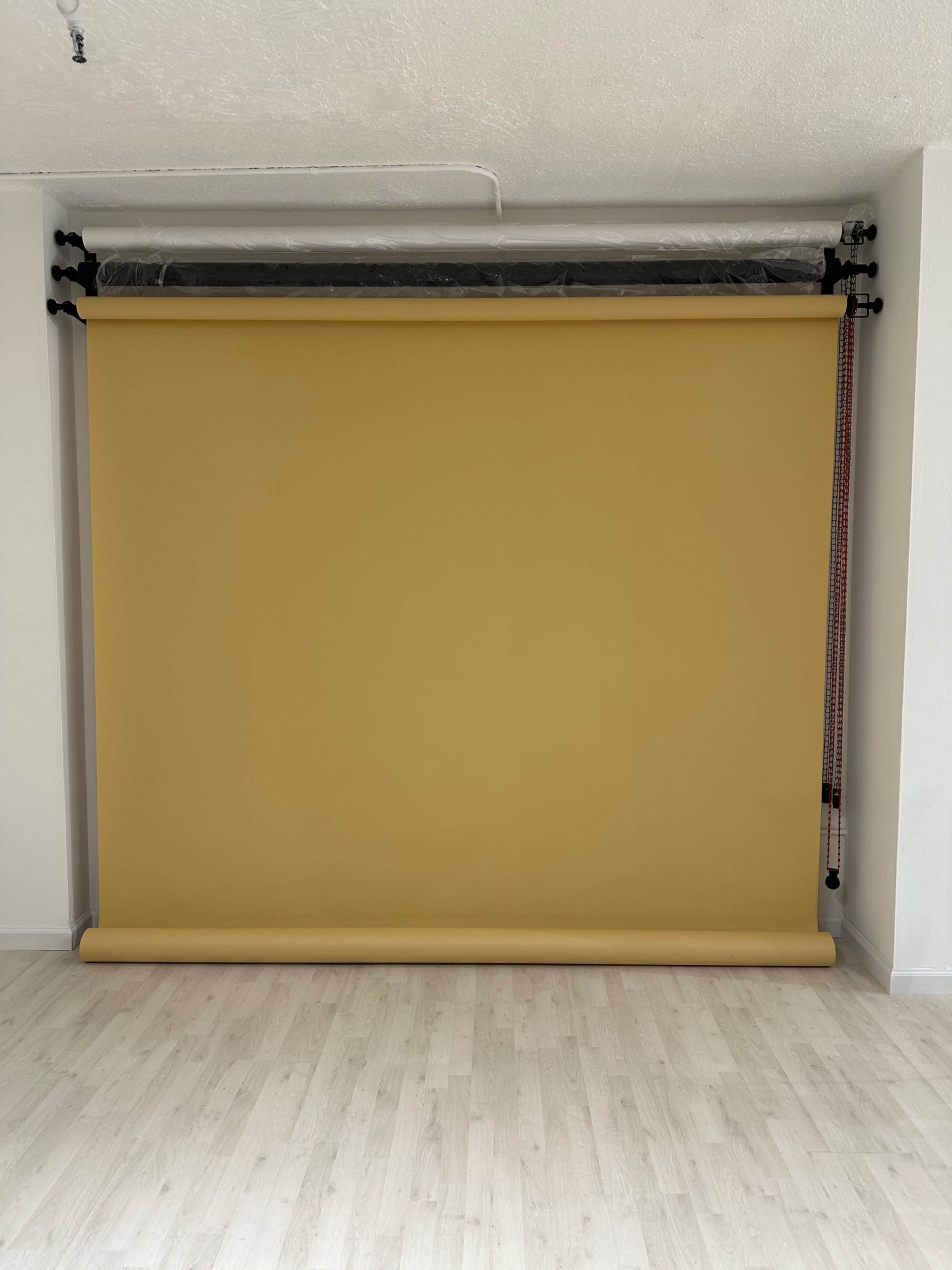 The image shows a plain yellow backdrop roll mounted on a wall in a room with light-colored flooring.