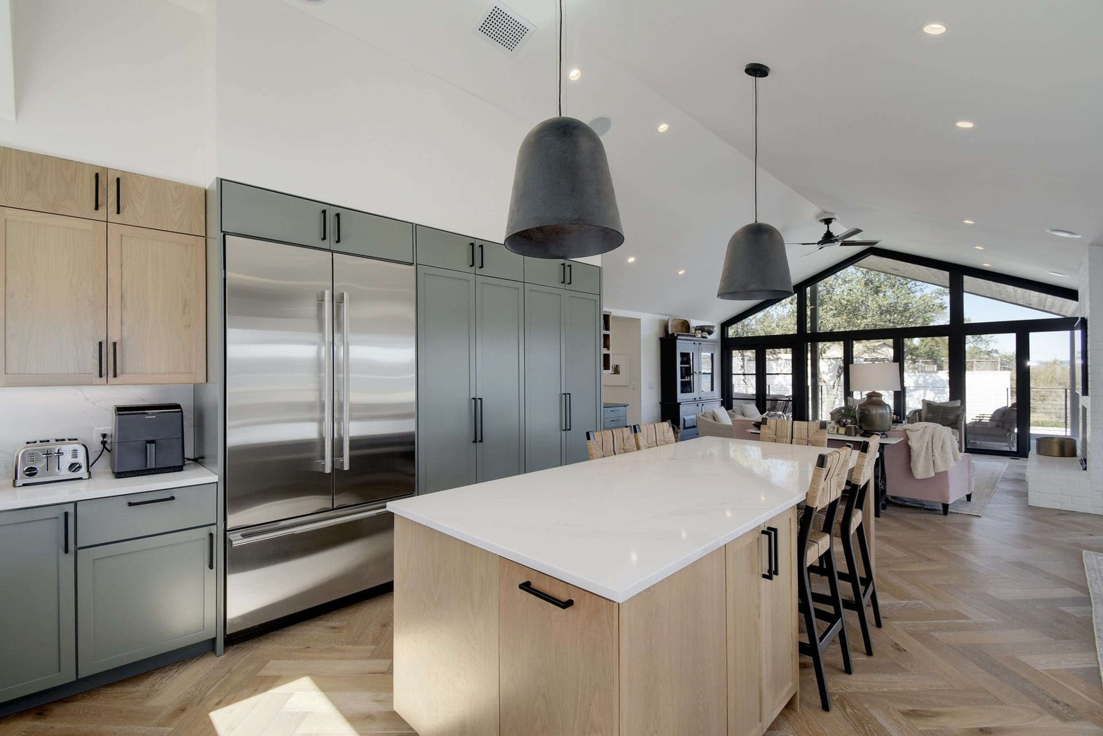 A modern kitchen featuring a large island with bar stools, stainless steel appliances, and a light wood cabinetry design under a vaulted ceiling.