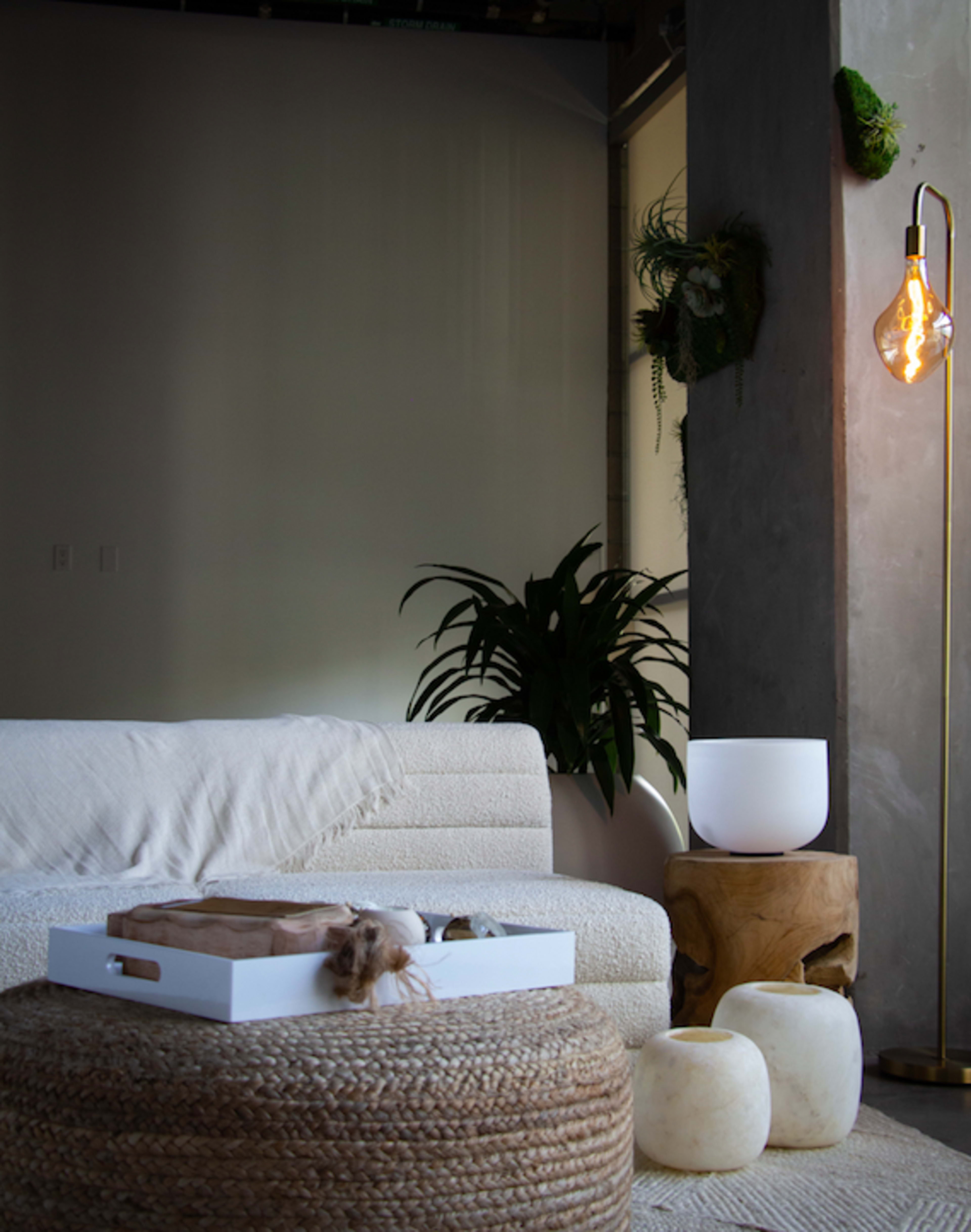 The scene shows a minimalist living room with a textured white sofa, a wooden side table, a woven rug, and warm lighting from a floor lamp.