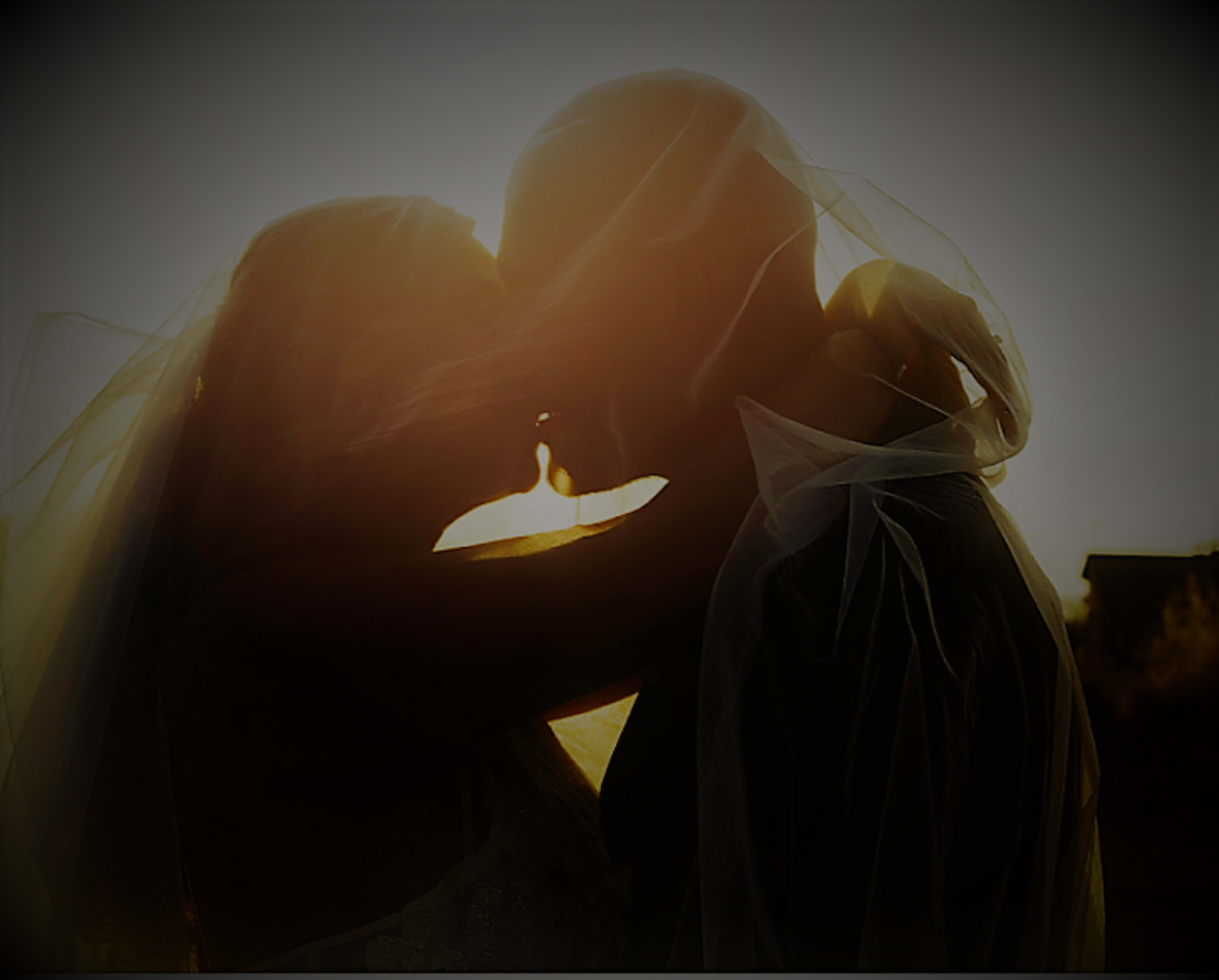 A couple shares a kiss at sunset, silhouetted against the glowing light.
