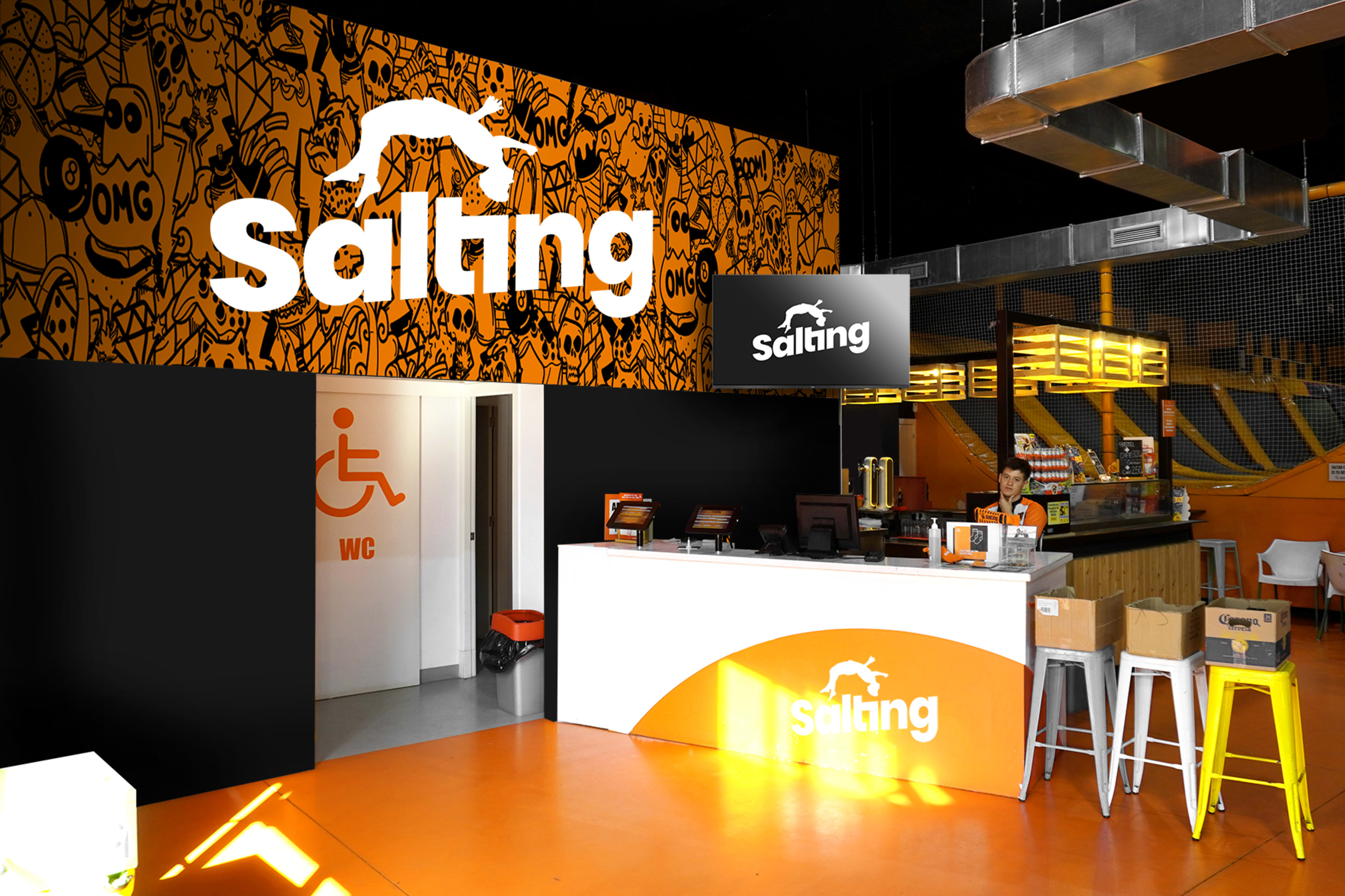 A brightly colored indoor space featuring a reception area with a counter, a sign displaying "Saltang," and a restroom entrance marked with a wheelchair symbol.