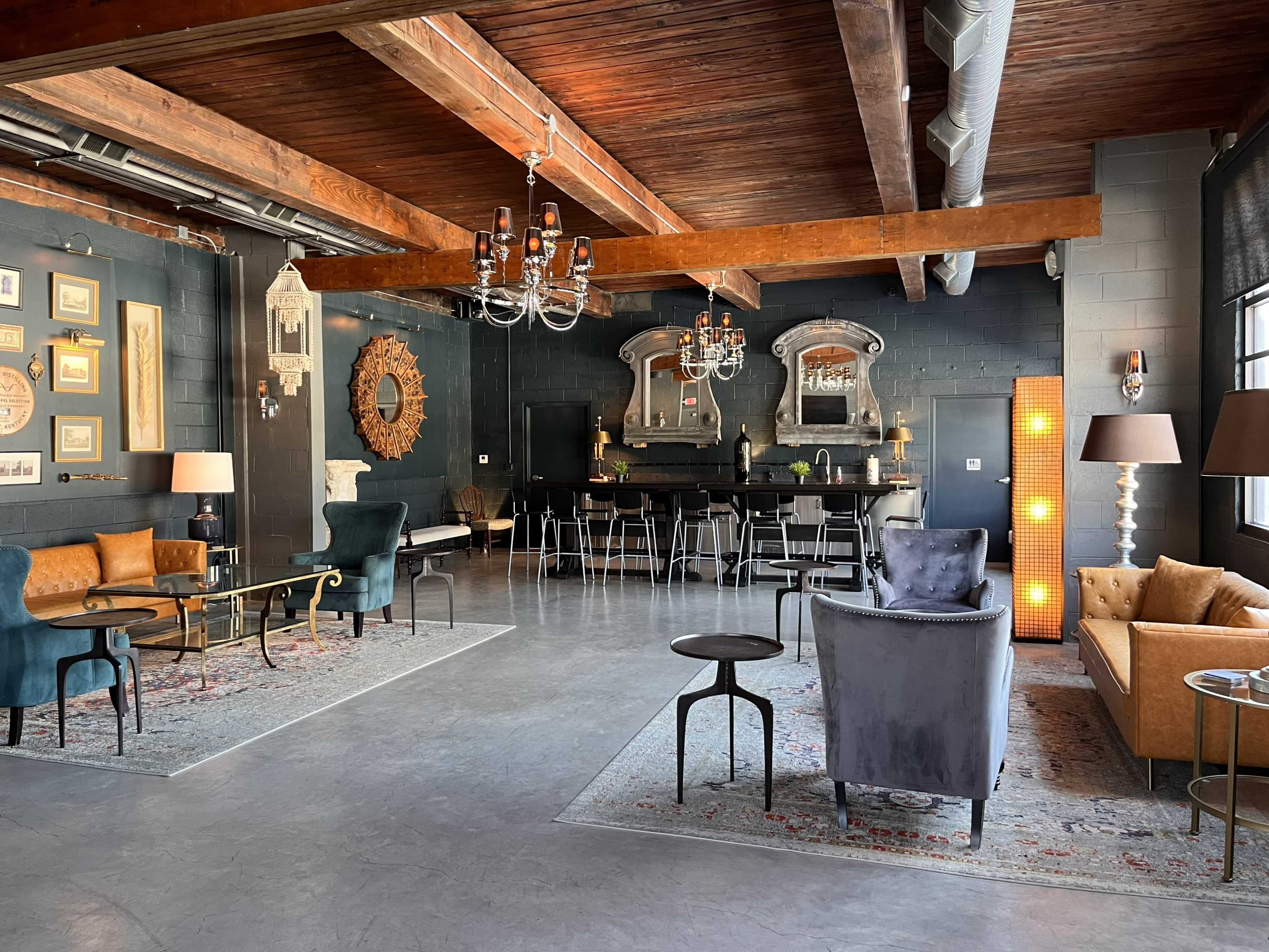 The image shows a stylish, open space with a mix of seating areas featuring various armchairs and sofas, a bar counter in the background, and decorative elements on the walls.