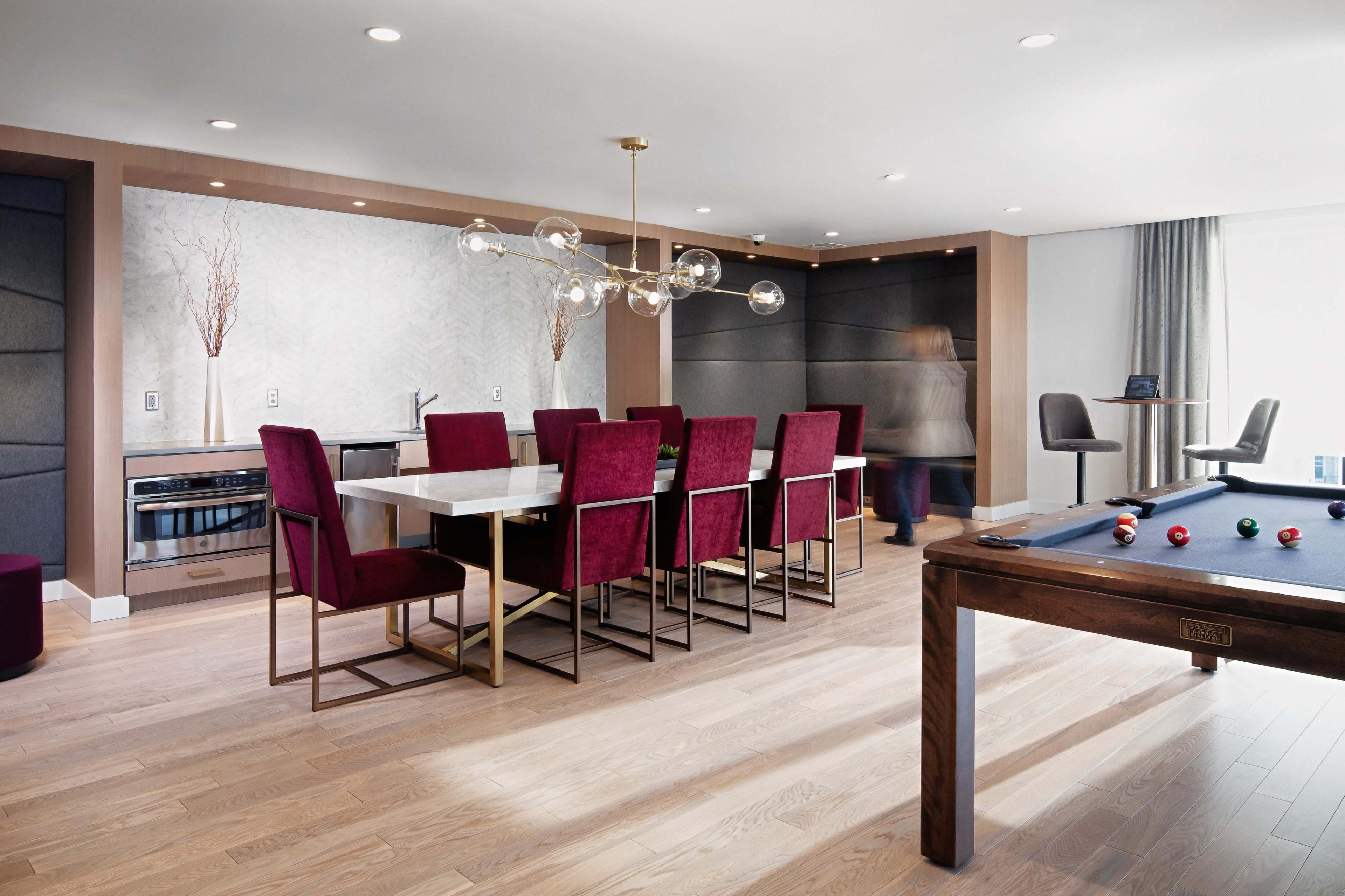 A modern dining area features a white marble table surrounded by burgundy chairs, with a pool table and contemporary lighting fixtures.