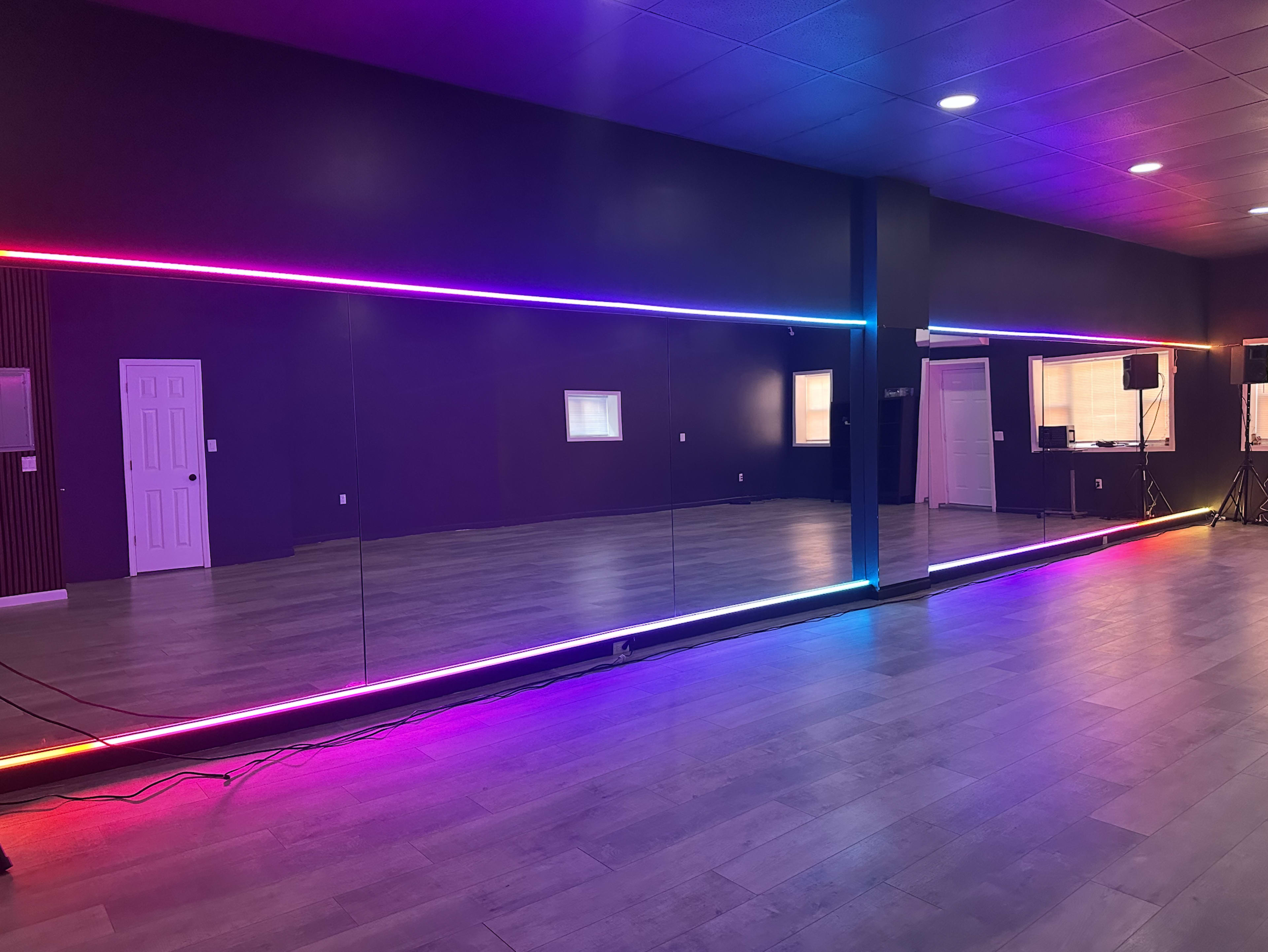 The image shows a spacious dance studio with a long mirror adorned with colorful LED lights along its edges.