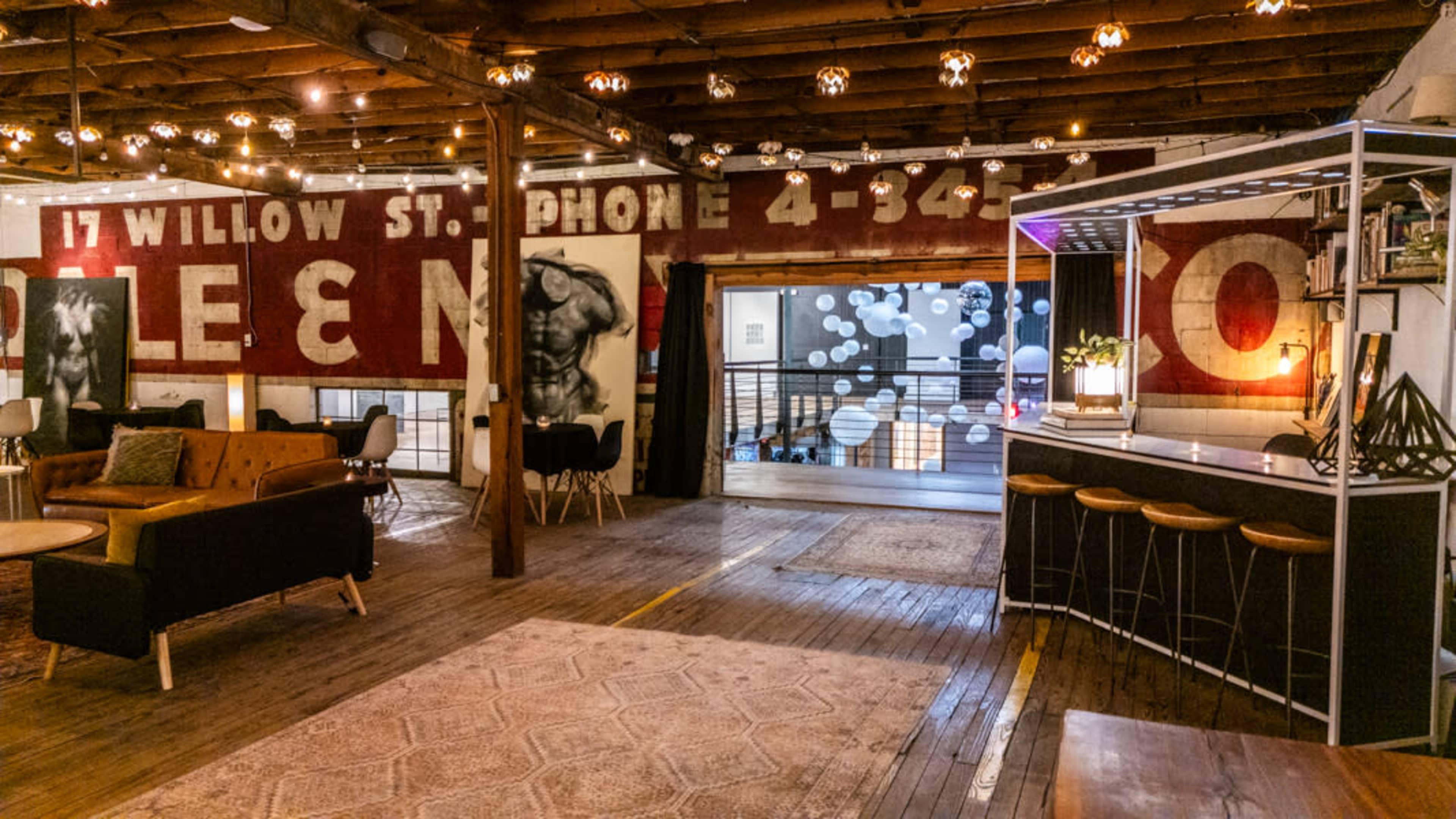 The interior features an open space with exposed wooden beams, vintage signage on the walls, and a bar area with modern furnishings.
