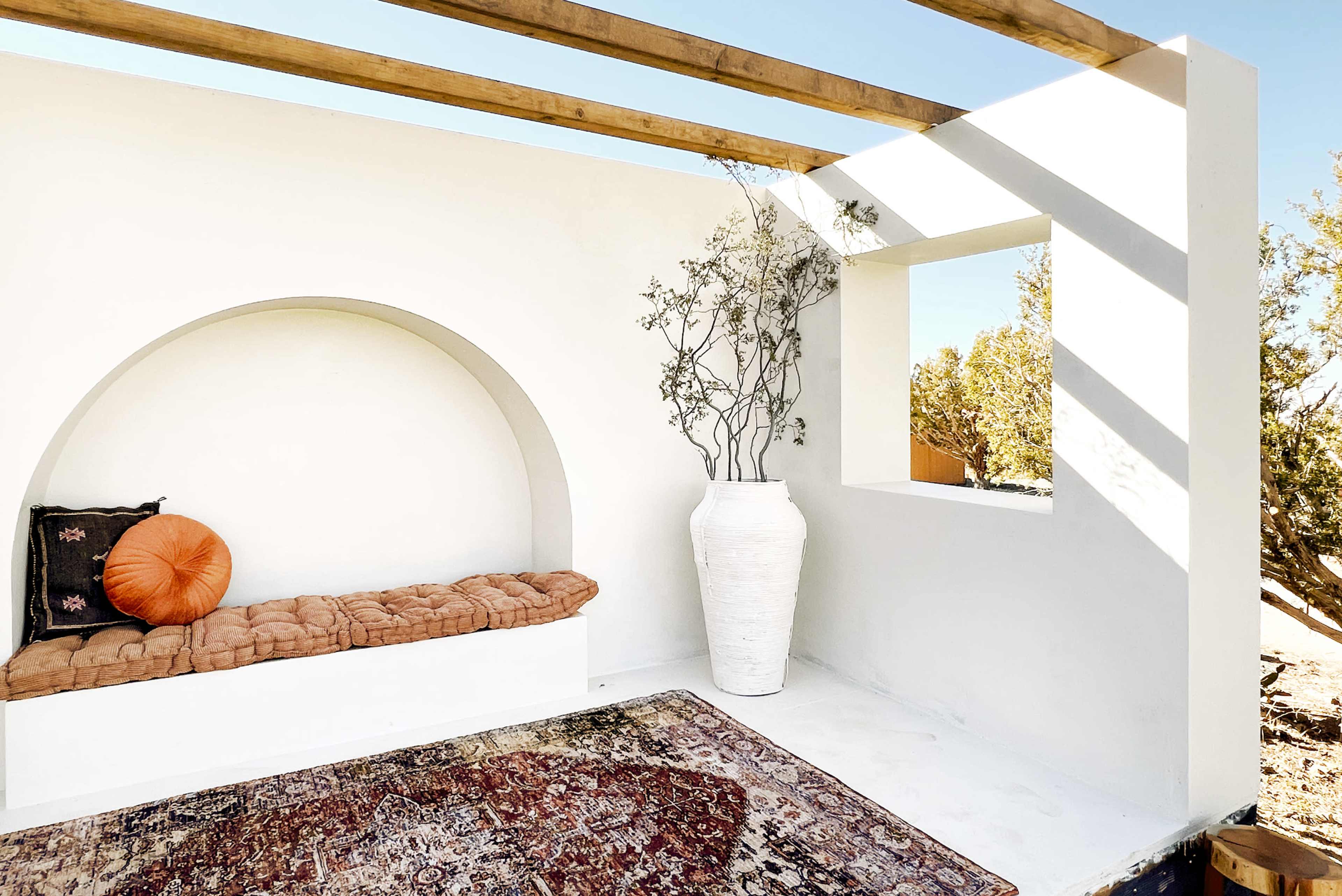 A minimalist indoor space with a cushioned seating area, a large white vase, and an opening that frames a view of the outdoors.
