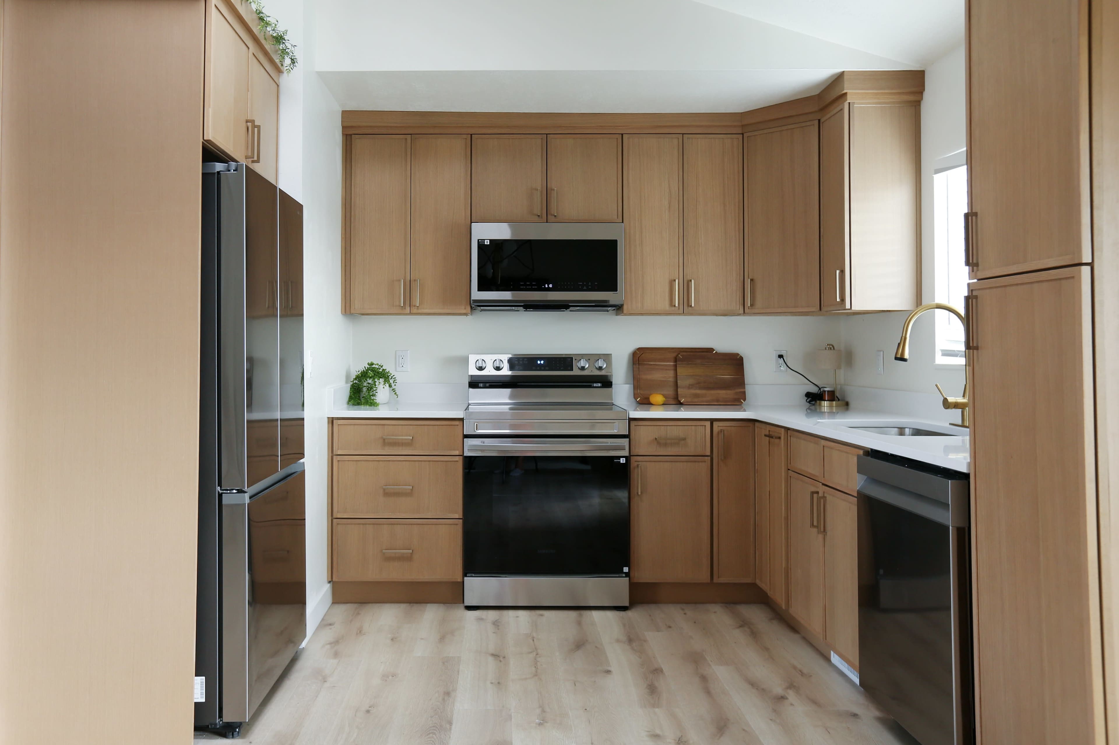 The image shows a modern kitchen with wooden cabinets, stainless steel appliances, and light-colored flooring.