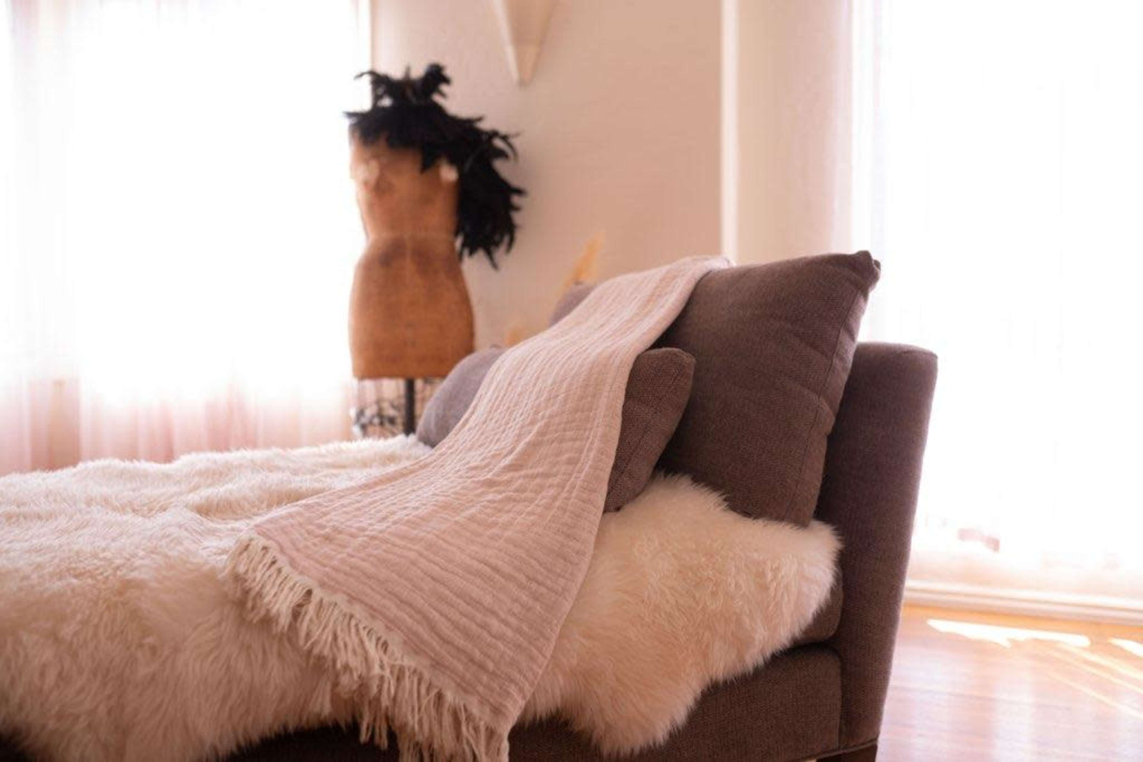 A cozy sofa draped with a fringed blanket sits beside a mannequin in a brightly lit room.