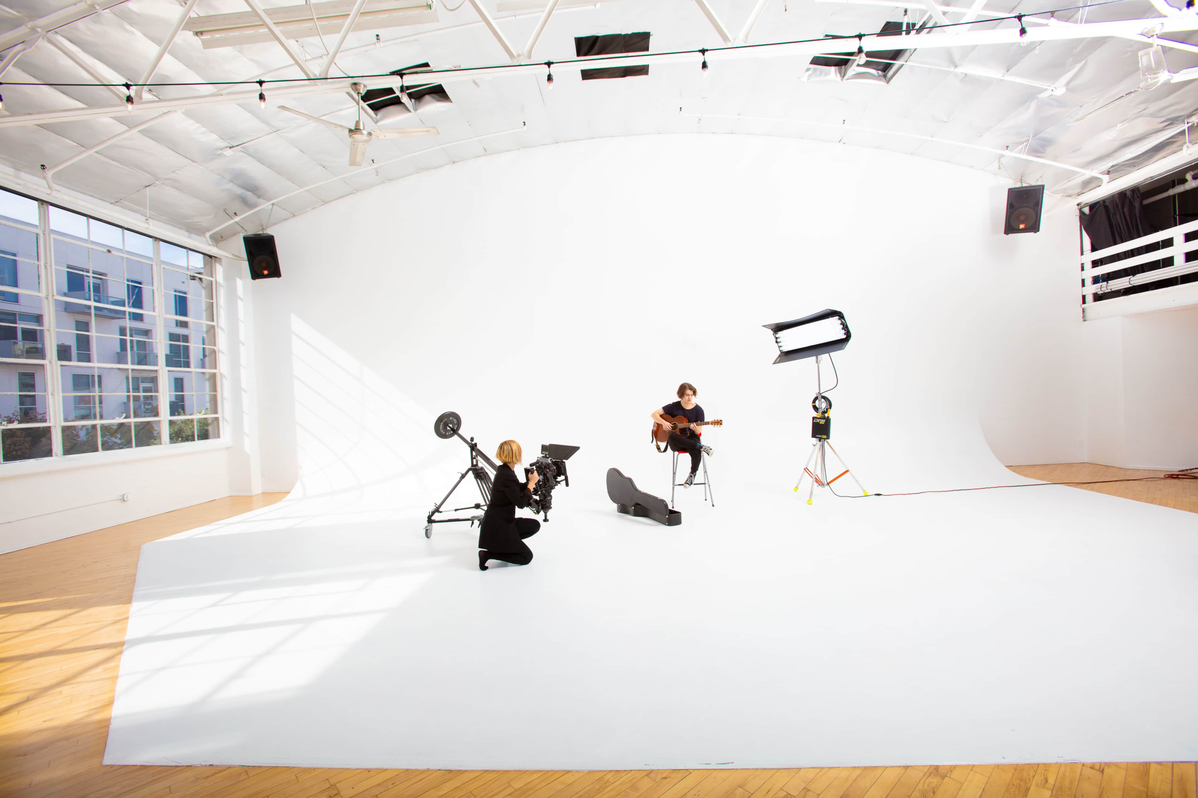 A photographer captures a musician playing guitar in a spacious, well-lit photo studio with a white backdrop.