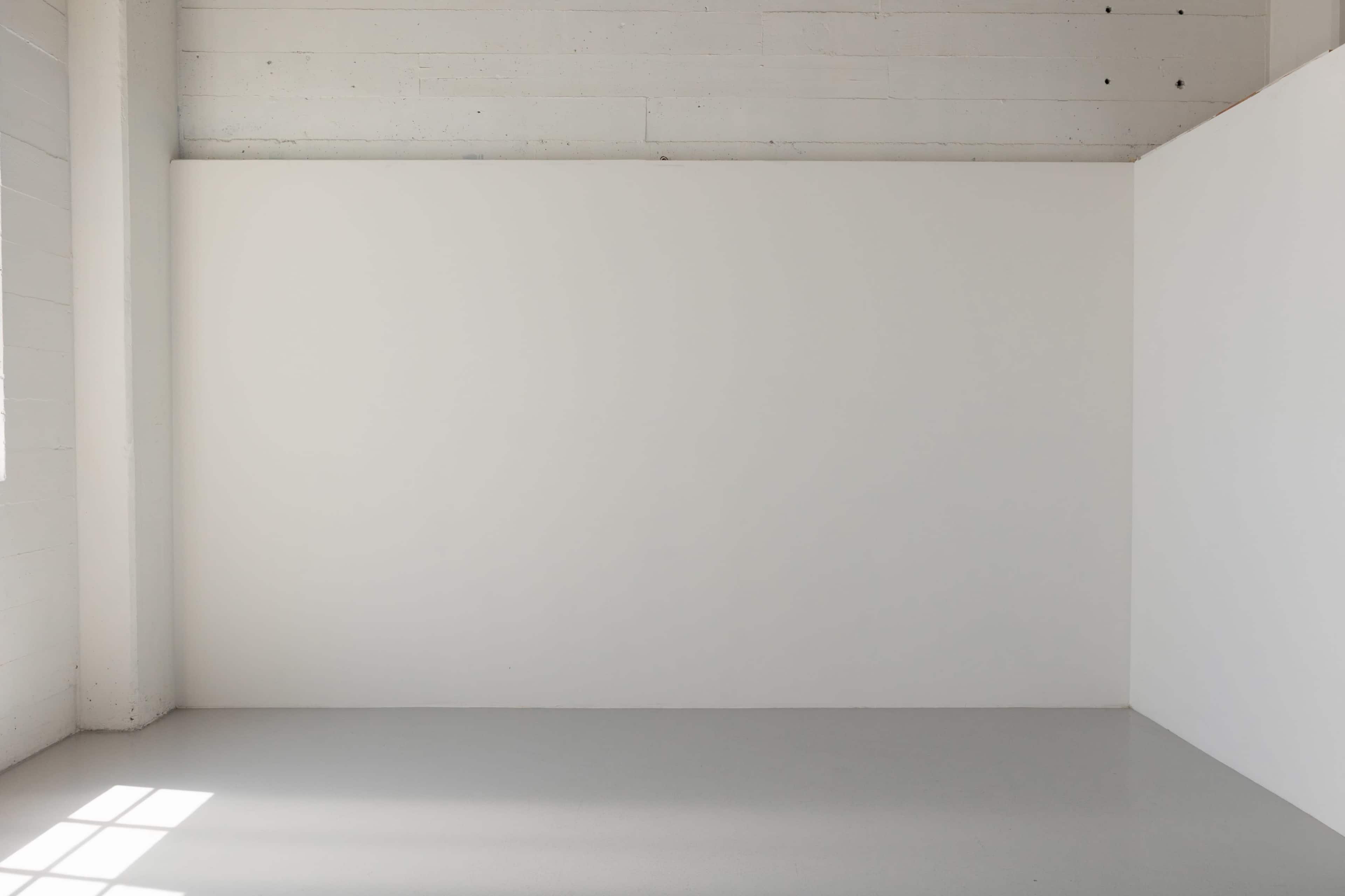 The image shows a minimalistic, bright room with a large white wall and a smooth gray floor.