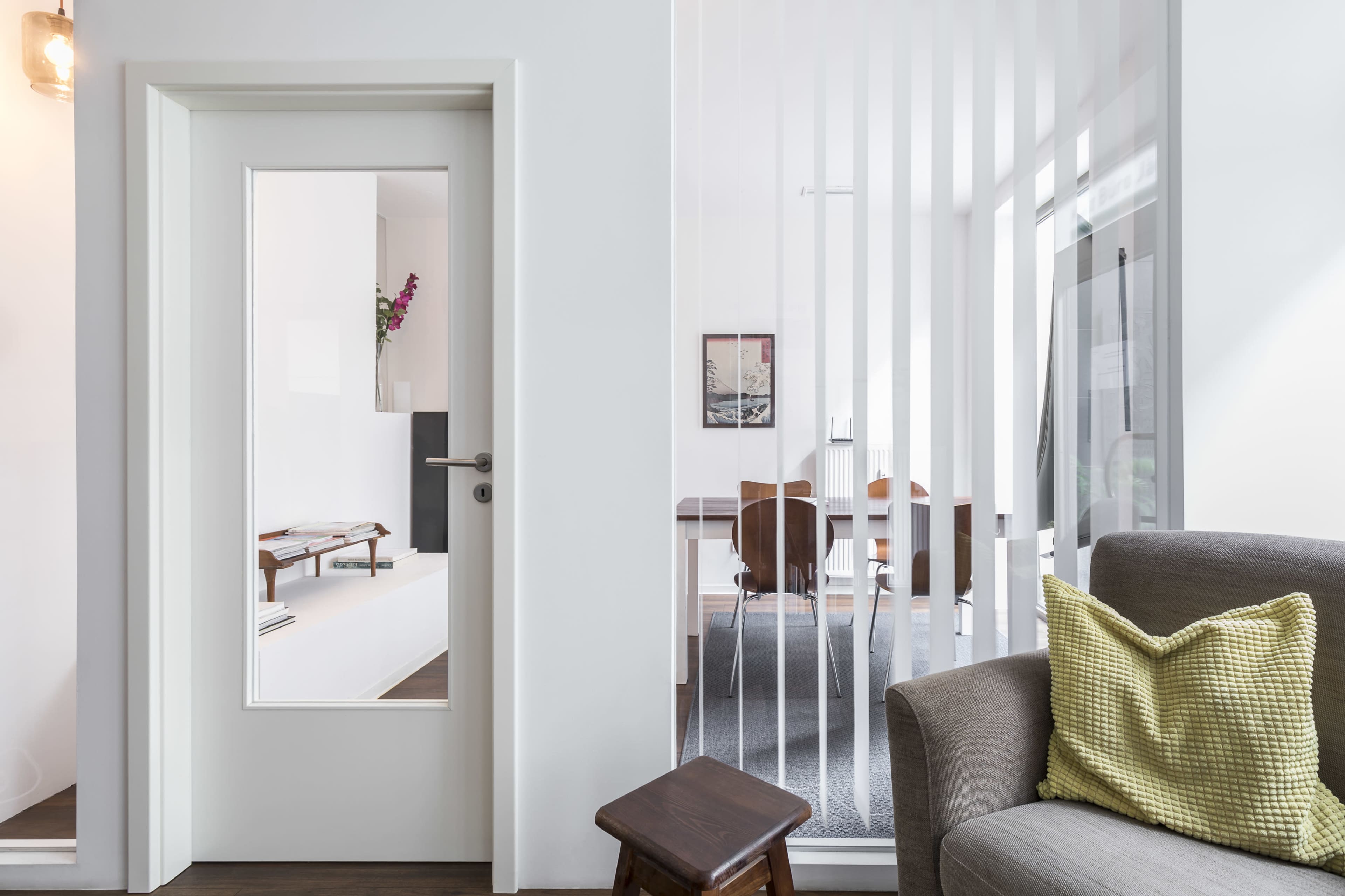 A modern living space features a door with a glass panel, leading to a room with a table and chairs visible in the background.