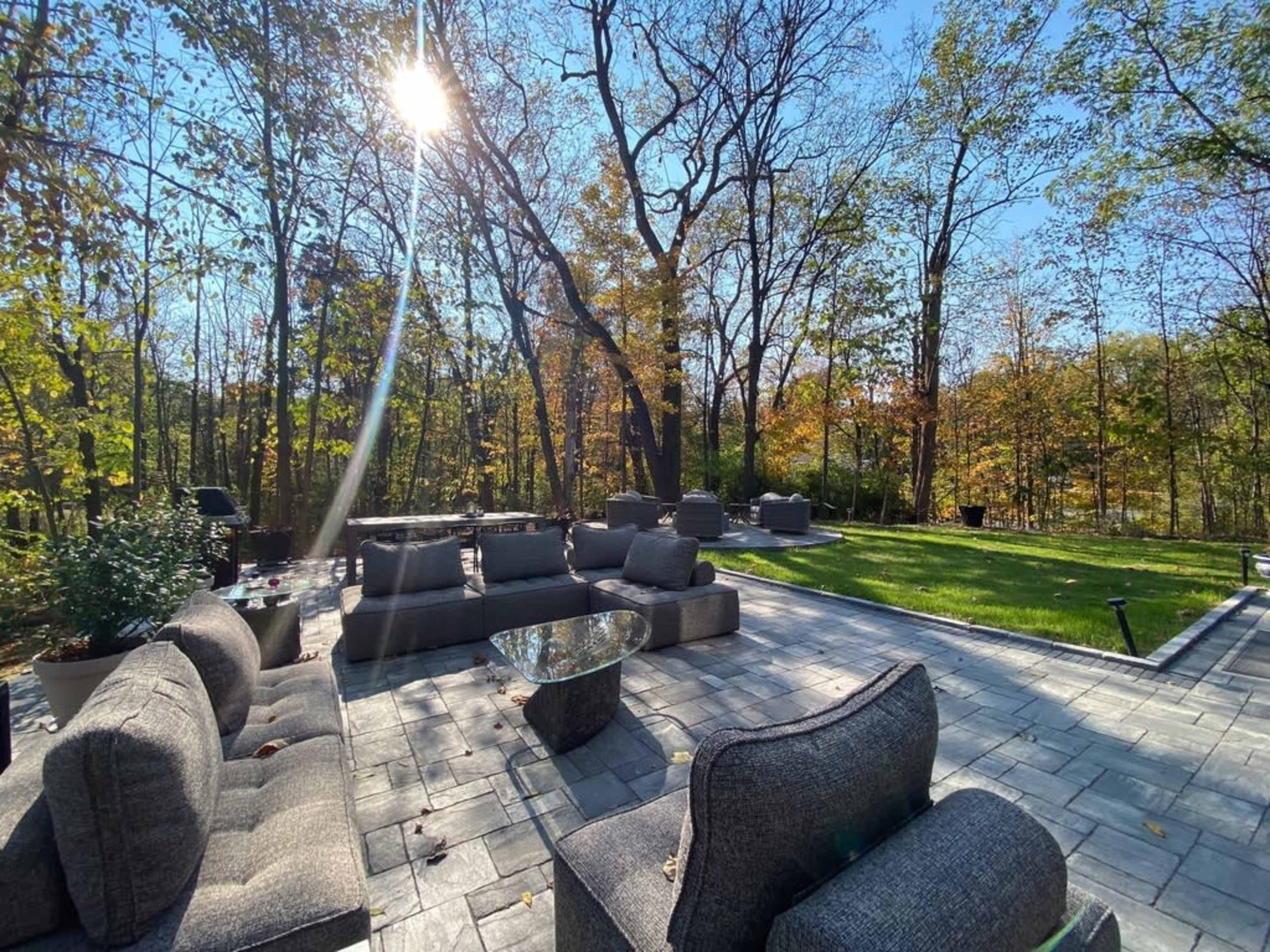 A patio area with modern outdoor furniture is set amidst a backdrop of trees, showcasing vibrant autumn foliage and a clear blue sky.
