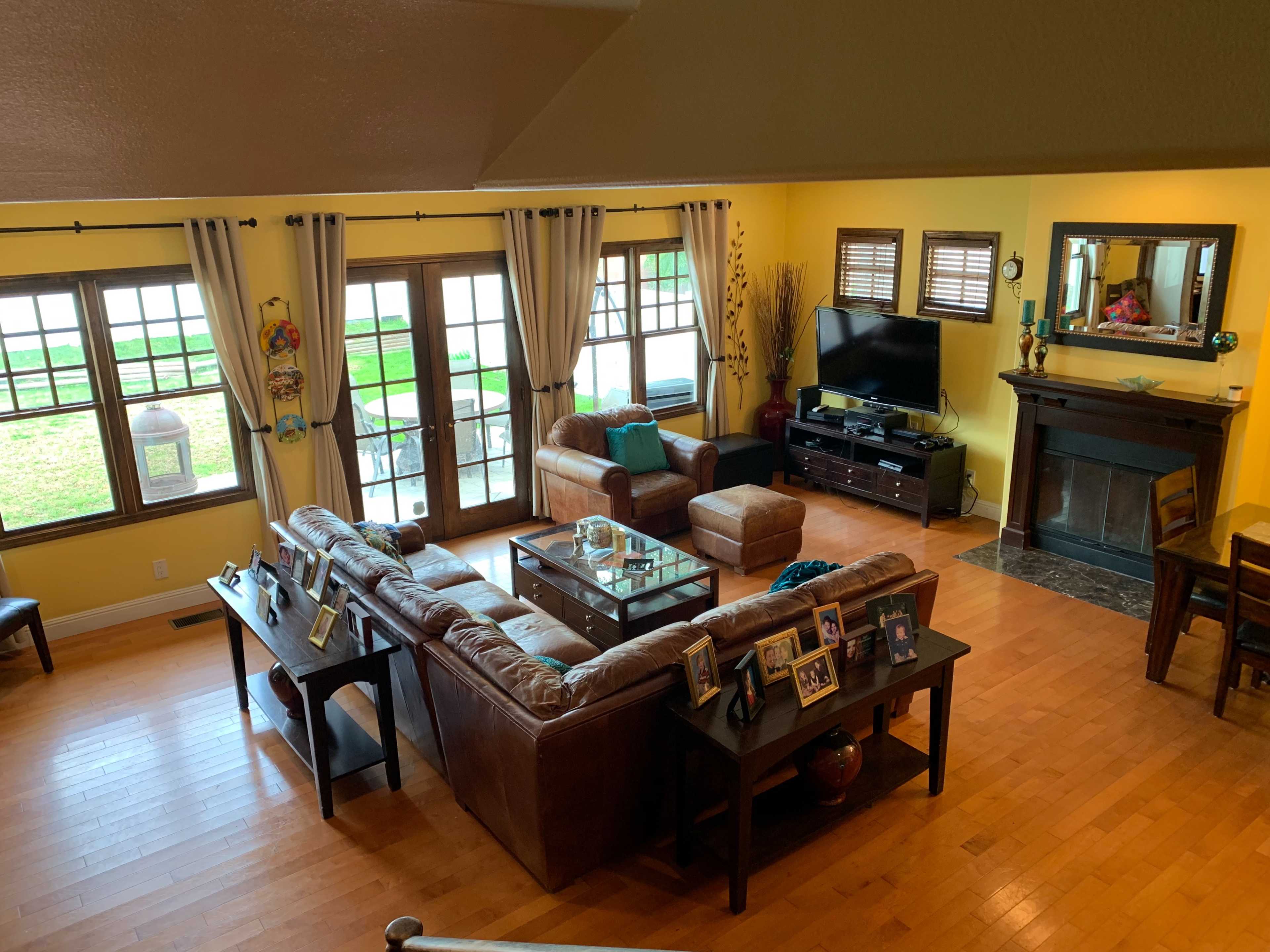 A spacious living room with a brown leather sectional sofa, a coffee table, and large windows overlooking a grassy area.
