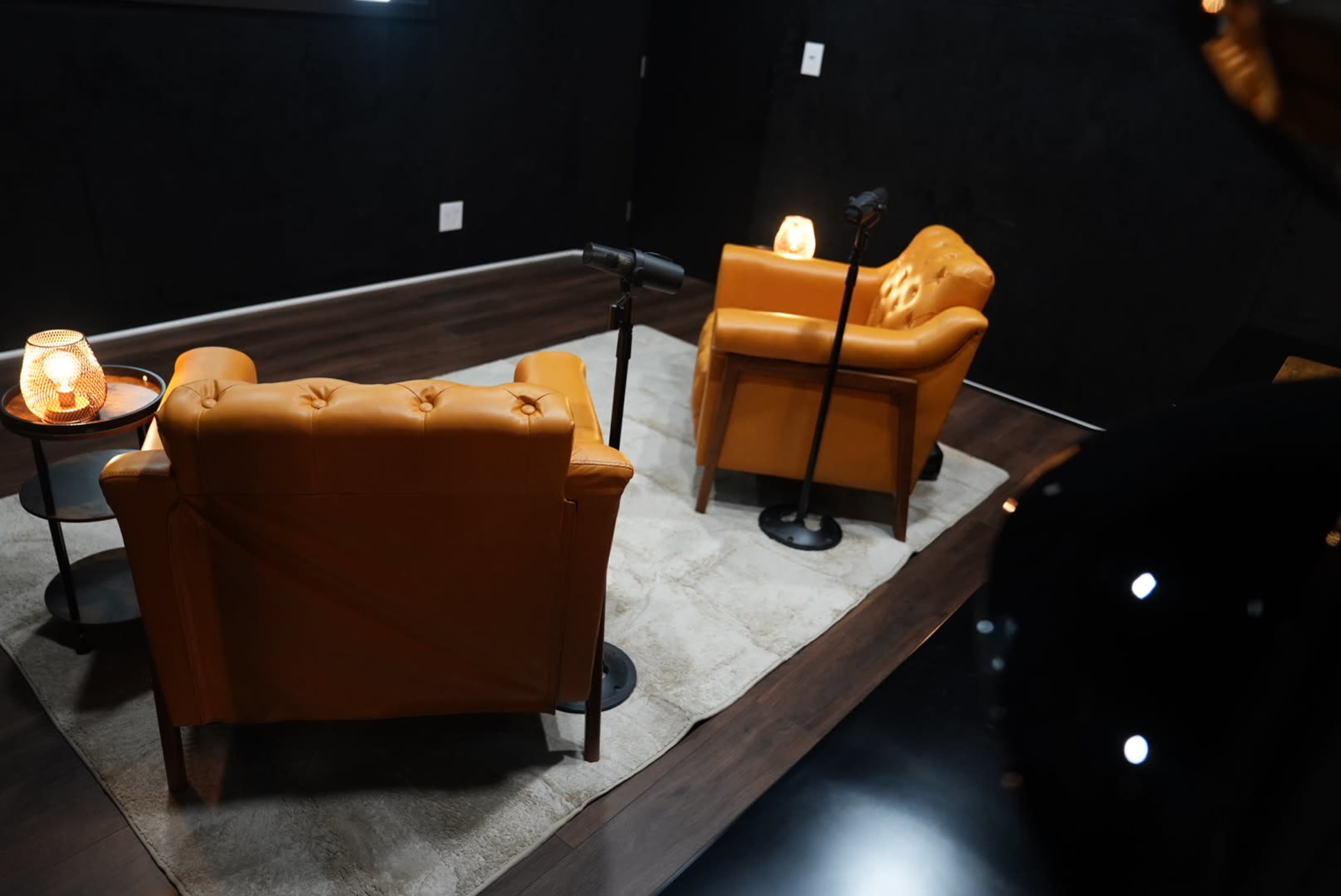 Two orange armchairs are positioned on a gray rug, facing each other, with a small table and lamps beside them in a dimly lit room.