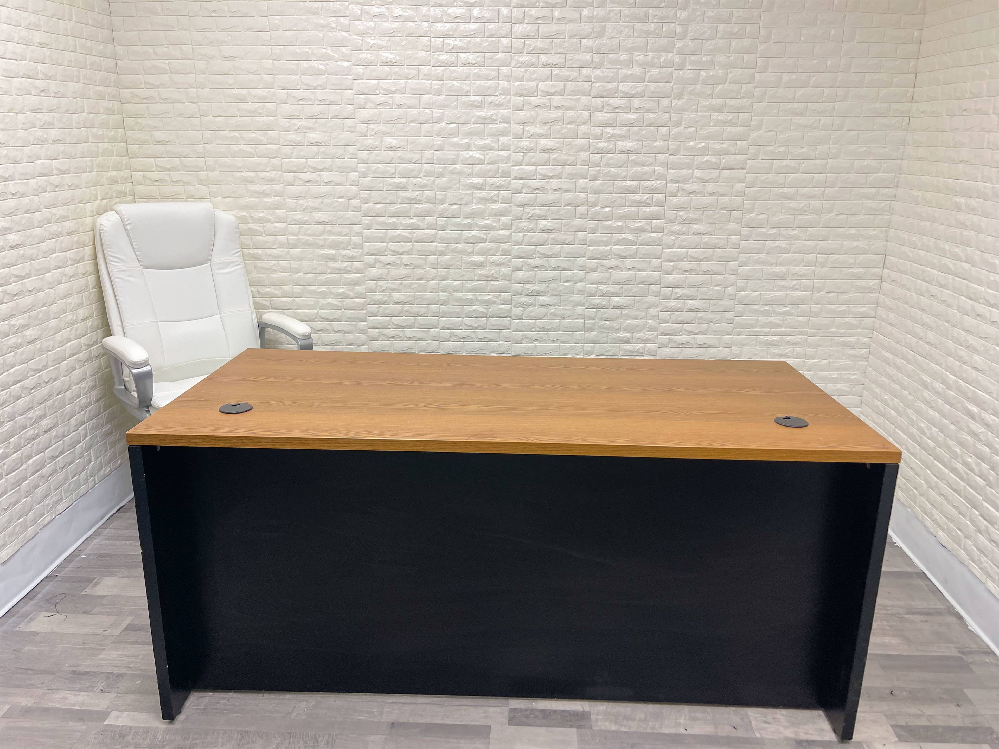 A plain office setting featuring a large wooden desk and a white ergonomic chair positioned against a textured white wall.